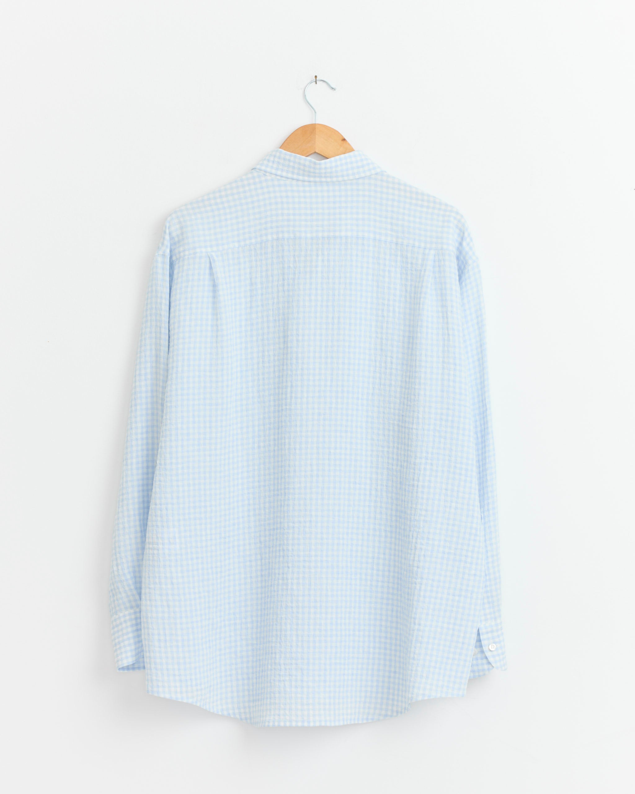 The Cale Water Twisted Linen Gingham Check Shirt in White/Blue hangs on a wooden hanger against a plain white wall, displayed from the back.