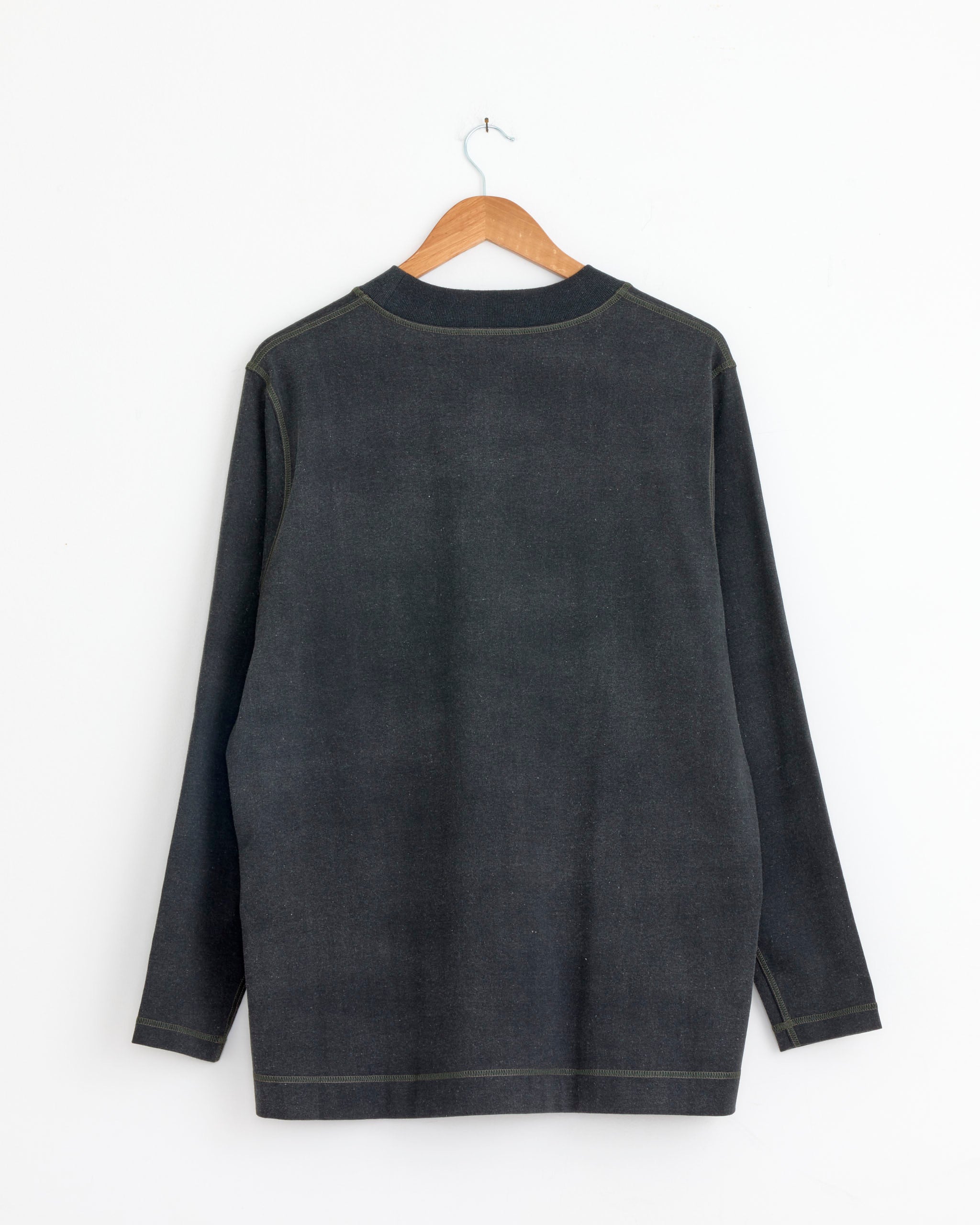 The Hollow Yarn Jersey Sweater in Grey Blue by Cale hangs on a wooden hanger against a plain white wall, shown from the back—check sizing details or use online chat for the perfect fit.
