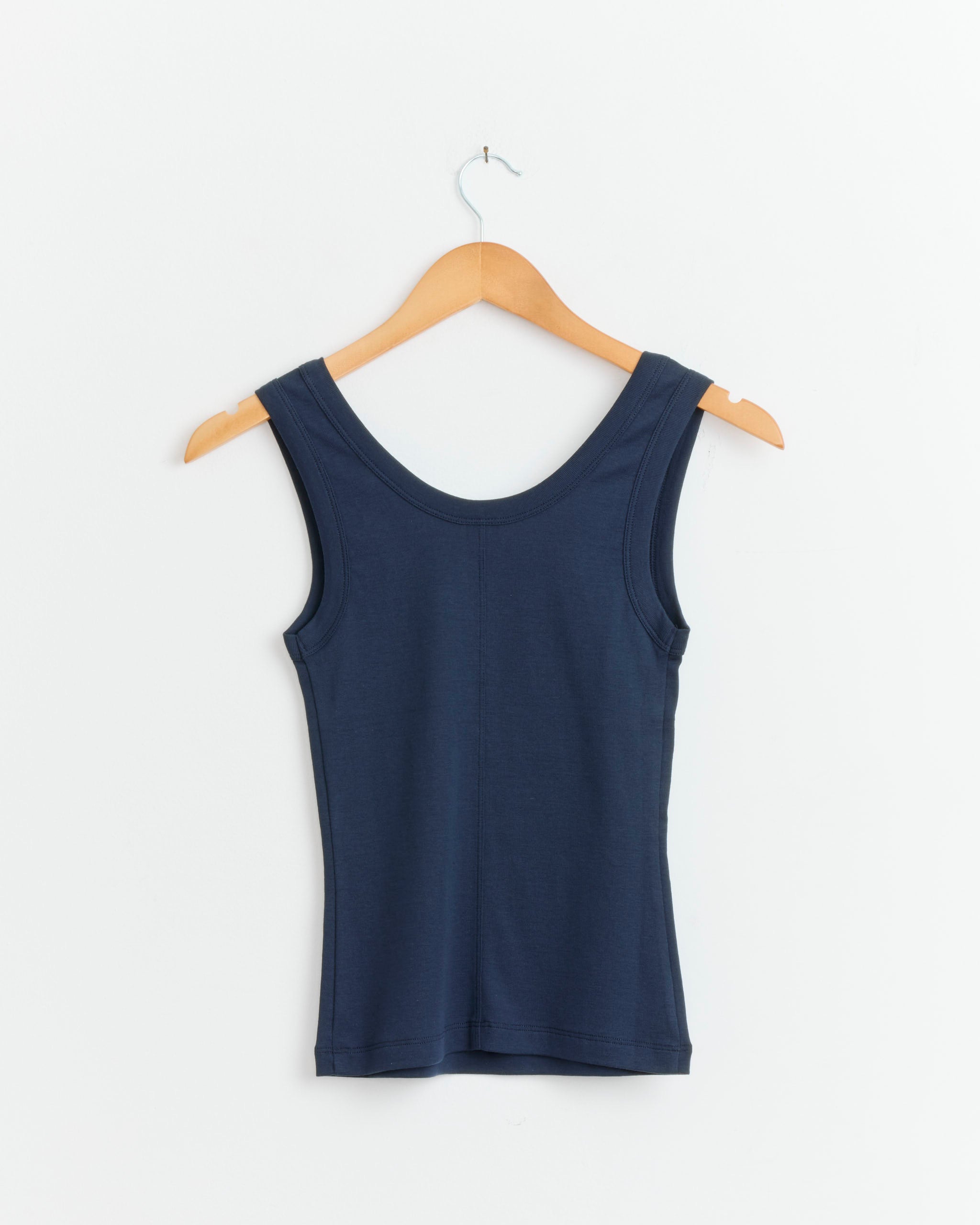 The Hillie Tank in Navy by FLORE FLORE, a fitted organic cotton scoop neck tank top, is displayed on a wooden hanger against a plain white wall.