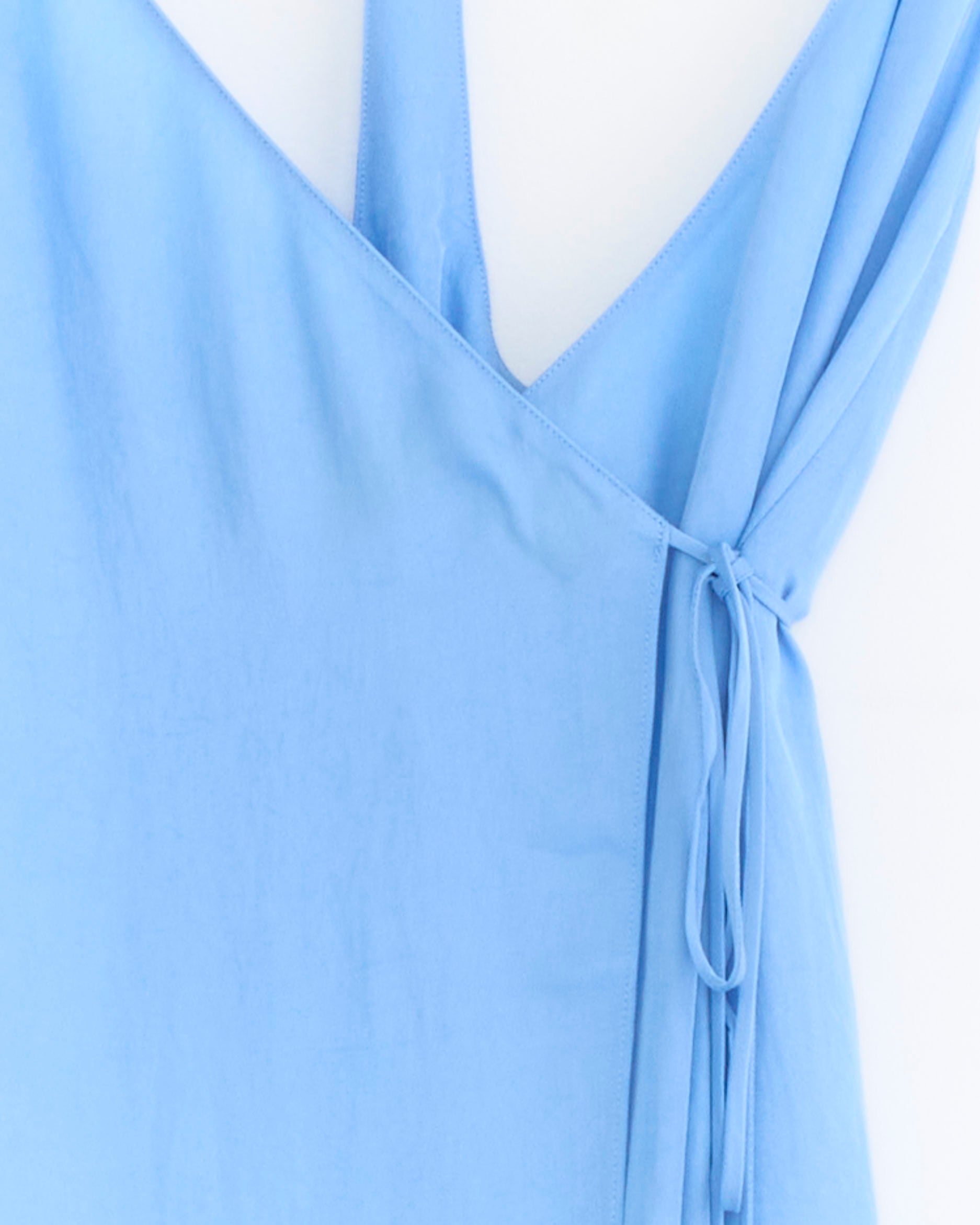 Close-up of the Tibi Slip Wrap Dress in Baby Blue, showcasing its V-neckline and adjustable fabric tie waist against a white background. This versatile wrap dress offers a flattering fit for any occasion.