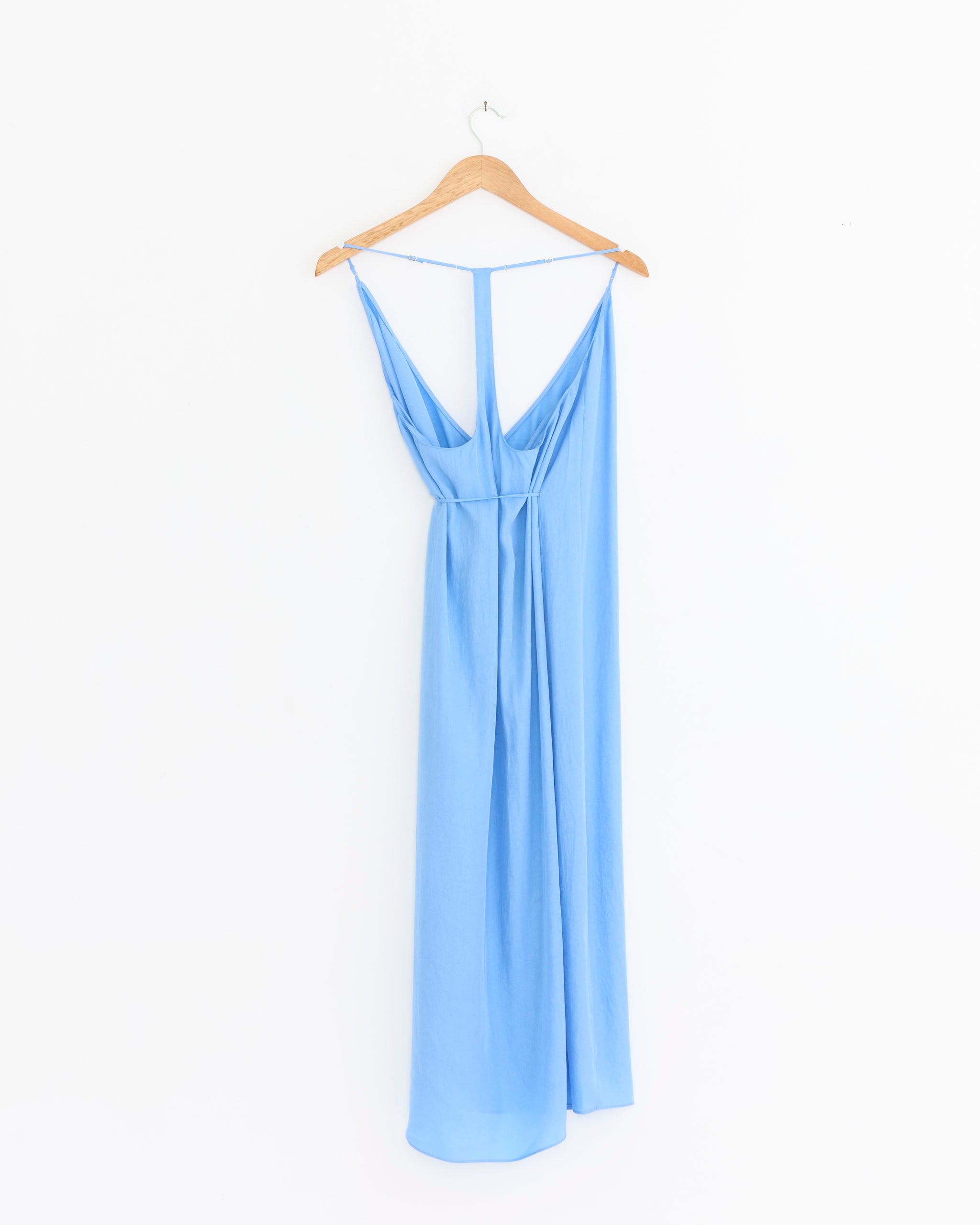 The Tibi Slip Wrap Dress in Baby Blue, featuring thin straps, a draped back, adjustable fit, and relaxed silhouette, hangs on a wooden hanger against a plain white background.