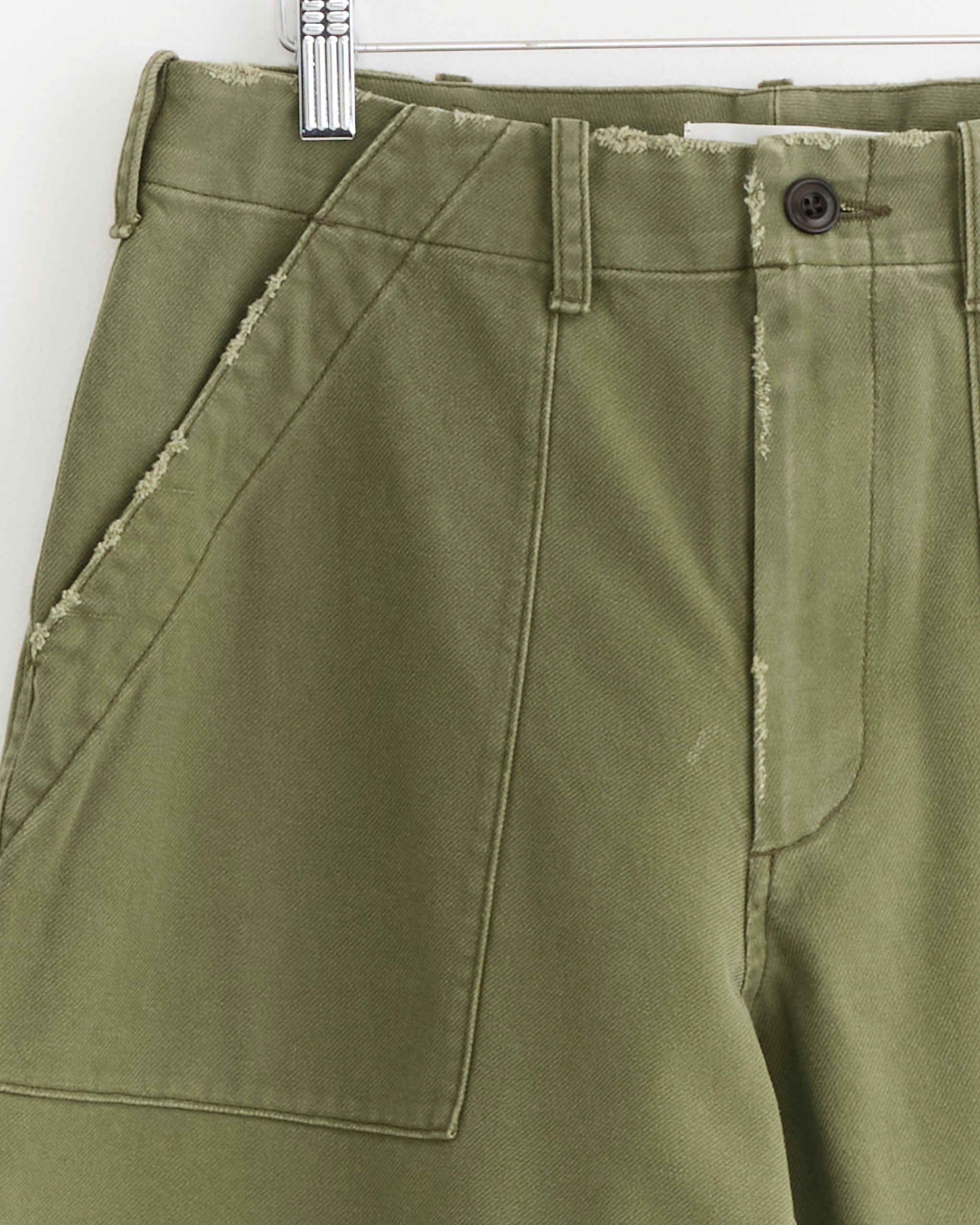 Close-up of the SMOCK Toyon Pant in French Cotton Twill Olive, featuring a relaxed straight-leg fit, visible waistband, button, belt loops, and a large front pocket with raw edges—a classic workwear-inspired piece.