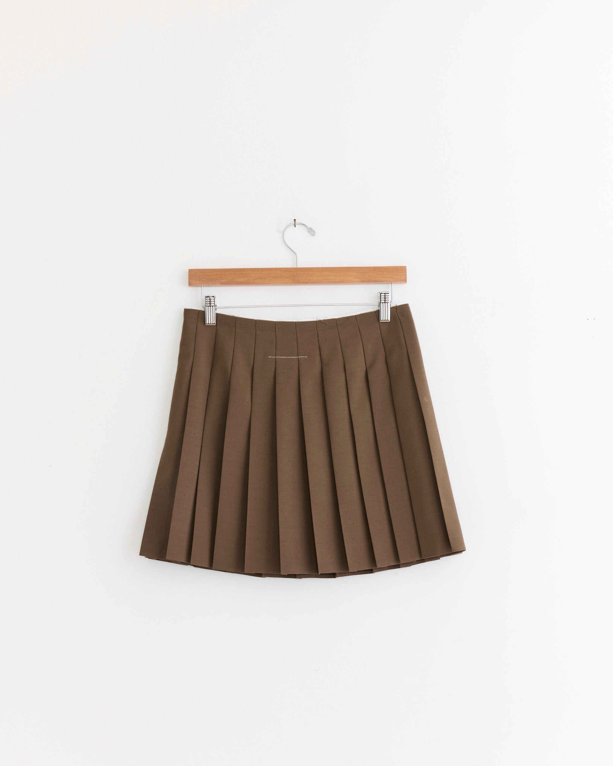 The MM6 Maison Margiela Mini Skirt in Brown hangs on a wooden hanger against a plain white wall.