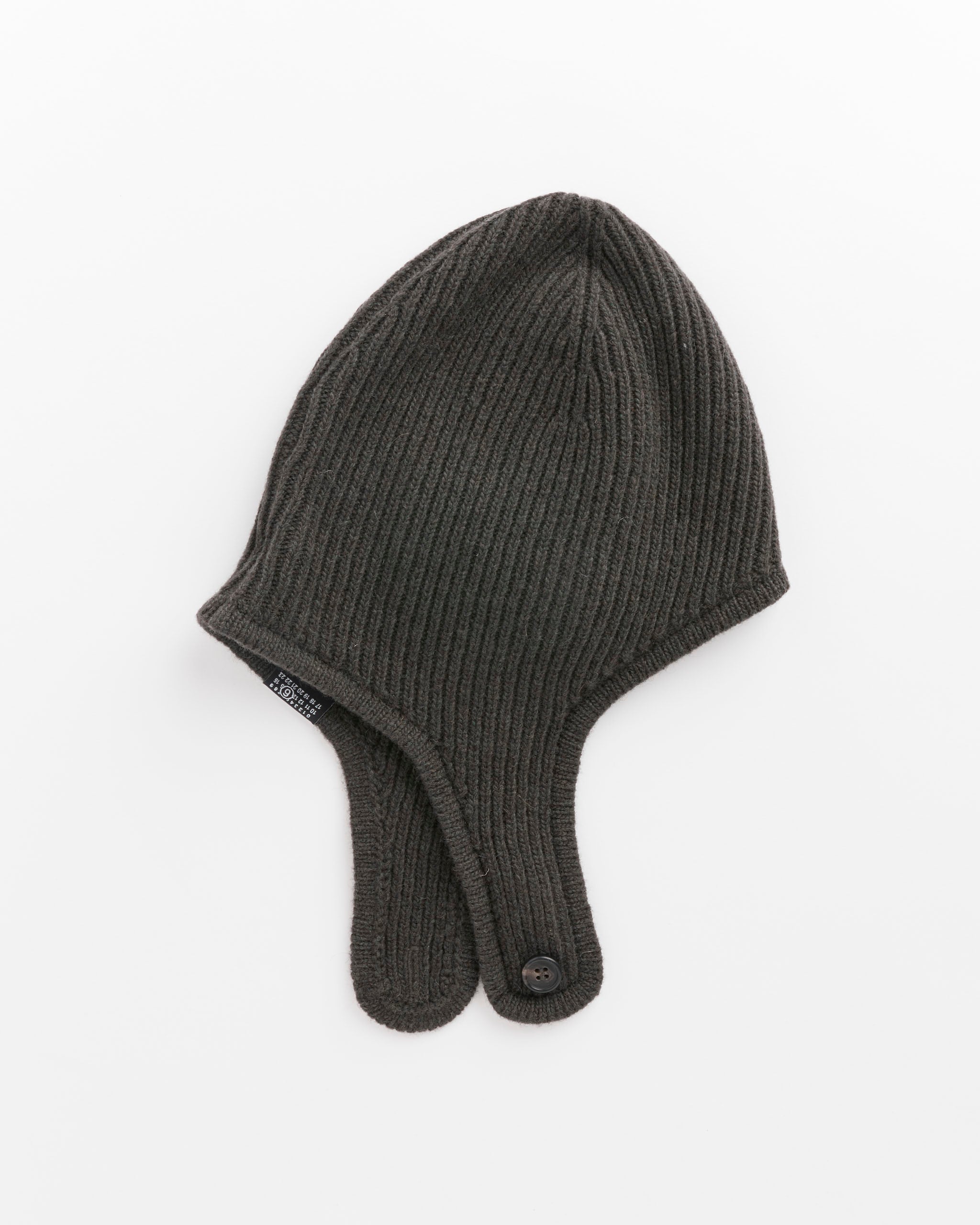 The Beanie in Khaki by MM6 Maison Margiela is a dark ribbed knit wool hat with two long ear flaps that button together at the ends, shown on a white background.