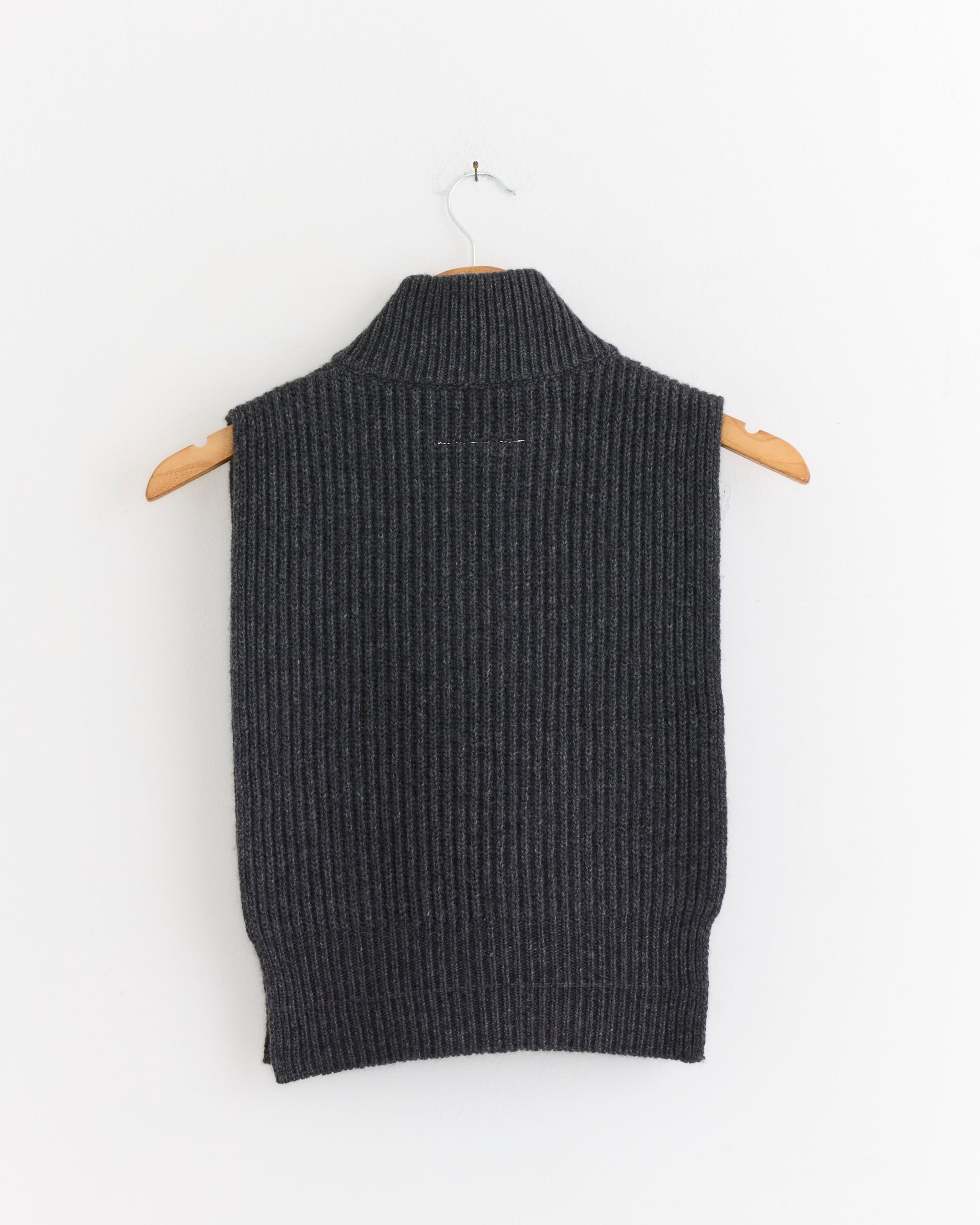 The MM6 Maison Margiela Wool Sweater Vest in Dark Grey Melange features a ribbed knit, high collar, and sleeveless cropped design. Shown on a wooden hanger against a white background.