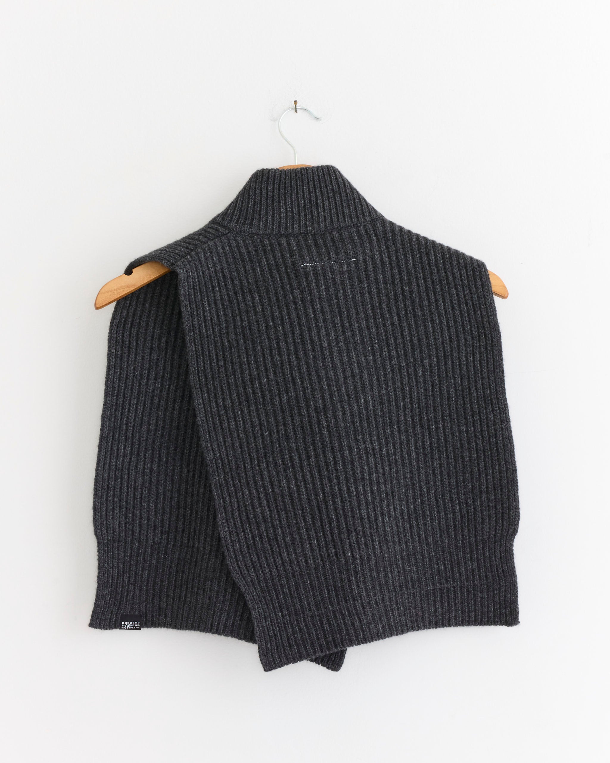 The MM6 Maison Margiela Wool Sweater Vest in Dark Grey Melange is shown on a wooden hanger against a plain white wall.