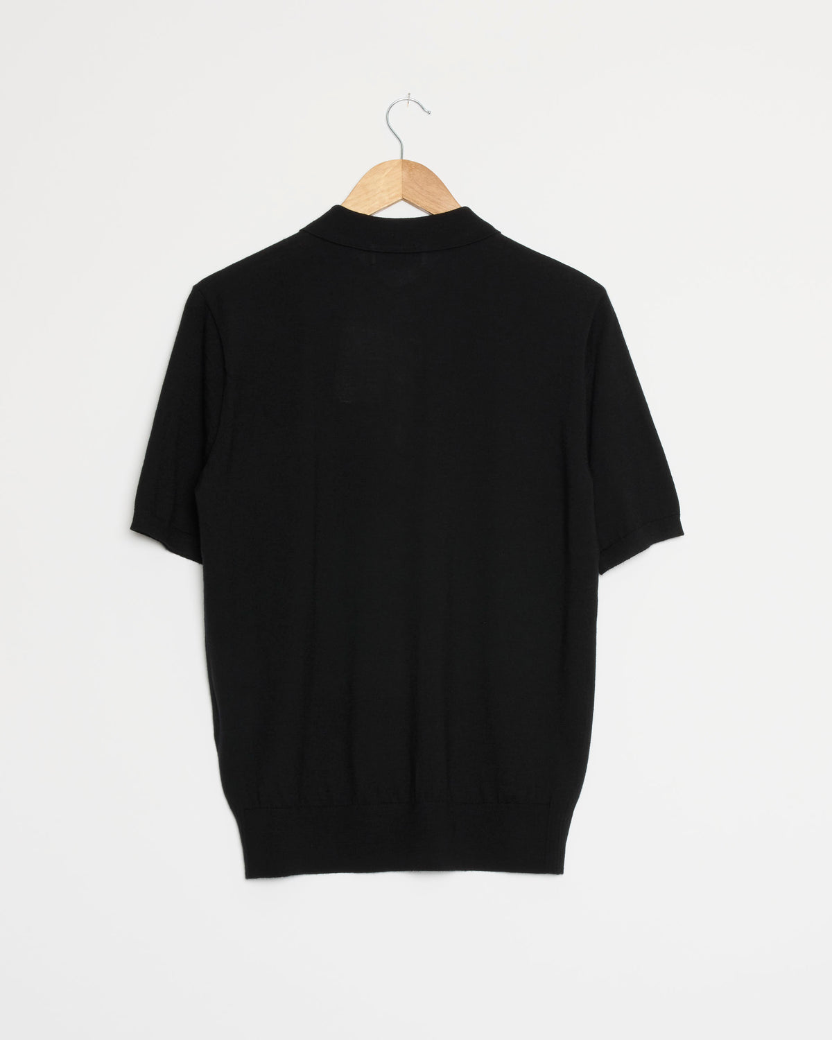 A black Wool Polo Sweater by Dries Van Noten, featuring short sleeves, is displayed on a wooden hanger against a plain white background with its back side visible.