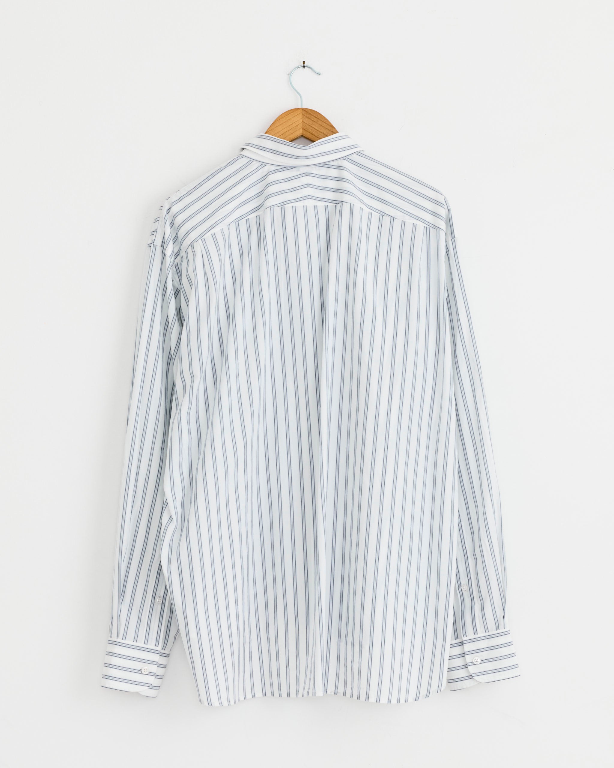 The Double Collar Shirt in Fine Blue Stripe by Salon C. Lundman, crafted from premium Italy Albini Cotton with thin blue stripes, hangs on a wooden hanger against a plain white wall, shown from the back.