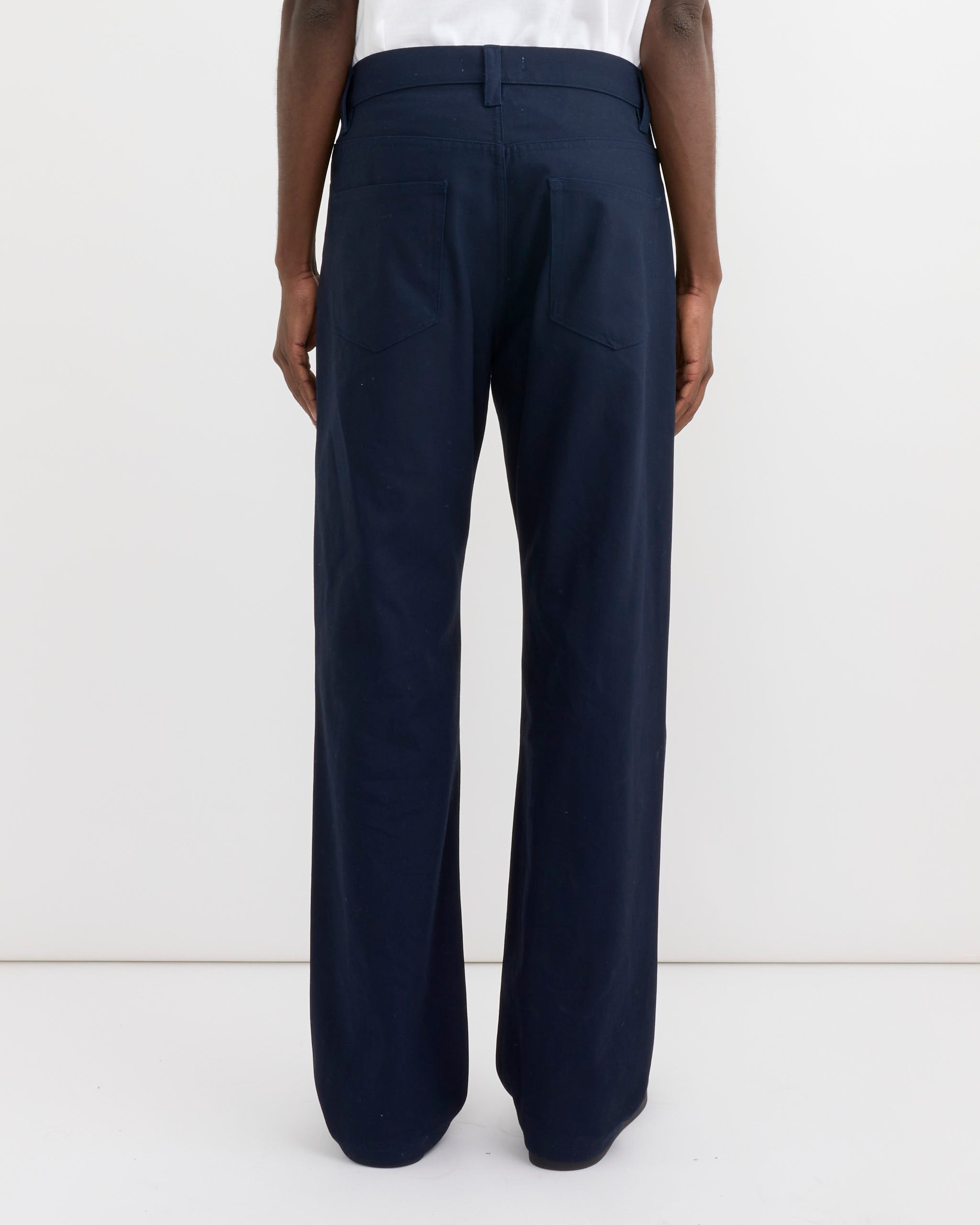 A person is seen from the back wearing SMOCK’s Ply Jean in Japanese Cotton Twill Navy, featuring wide legs, back pockets, and a waistband with belt loops, set against a plain white background.