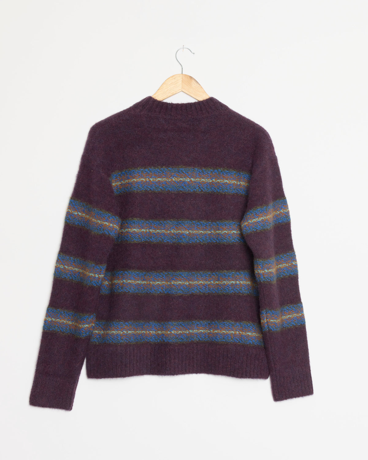 The Striped Sweater in Purple by Dries Van Noten, featuring blue and yellow horizontal stripes in a jacquard knit, hangs on a wooden hanger against a plain white background.