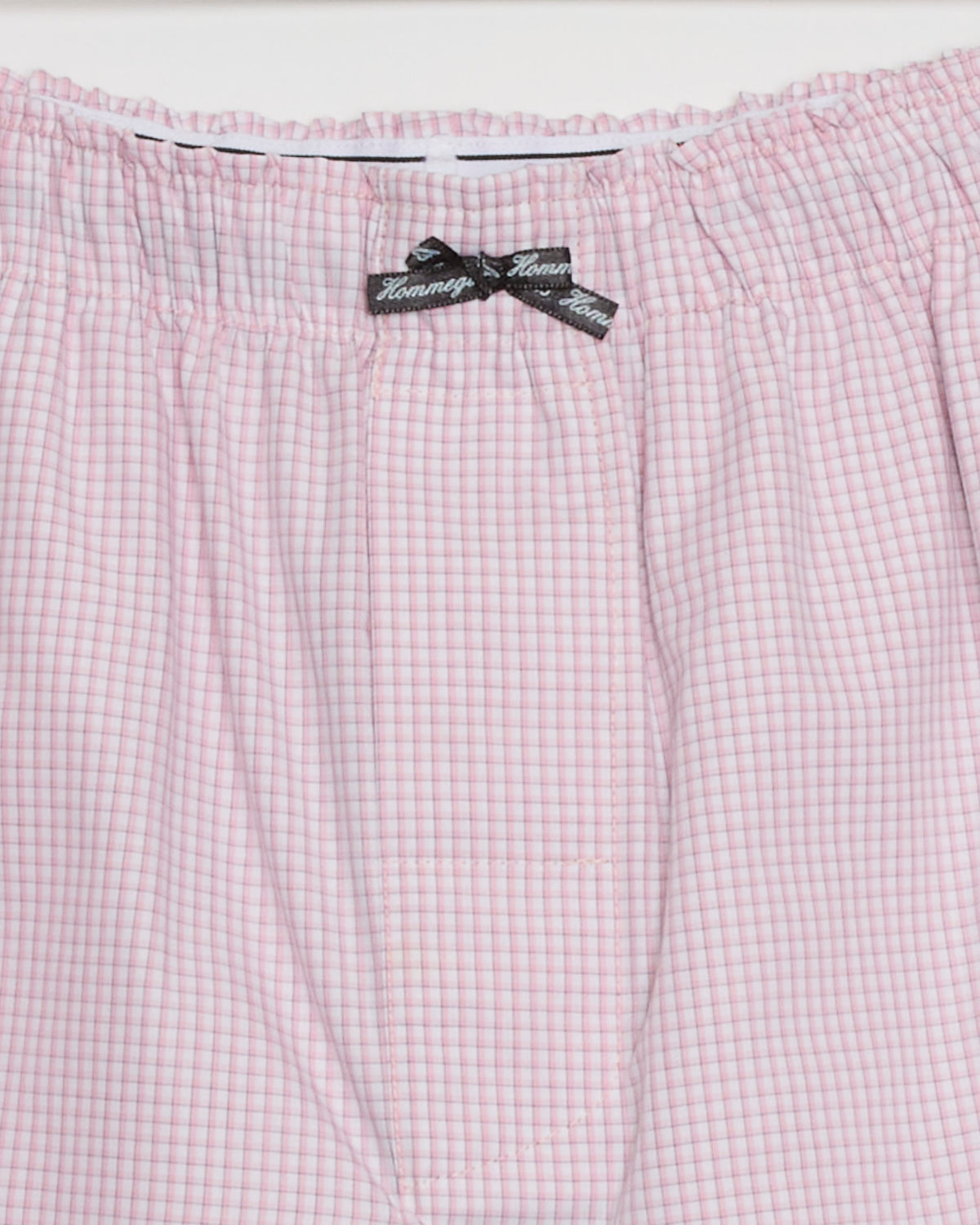 Close-up of the waistband of the Long Boxer Short in Pink Graph by Hommegirls, crafted from 100% cotton for comfort. A small black bow at the center is adorned with repeating “Tommy” lettering. The playful pink graph pattern lends a charming touch to these classic boxer shorts.