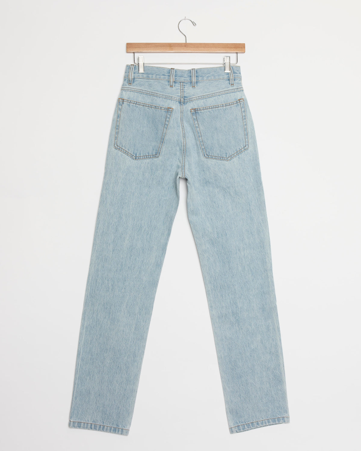 Light blue, high-waisted straight-leg jeans—the 1 Jean in Stonewash from Hommegirls—are displayed from the back, hanging on a wooden hanger against a plain white background.