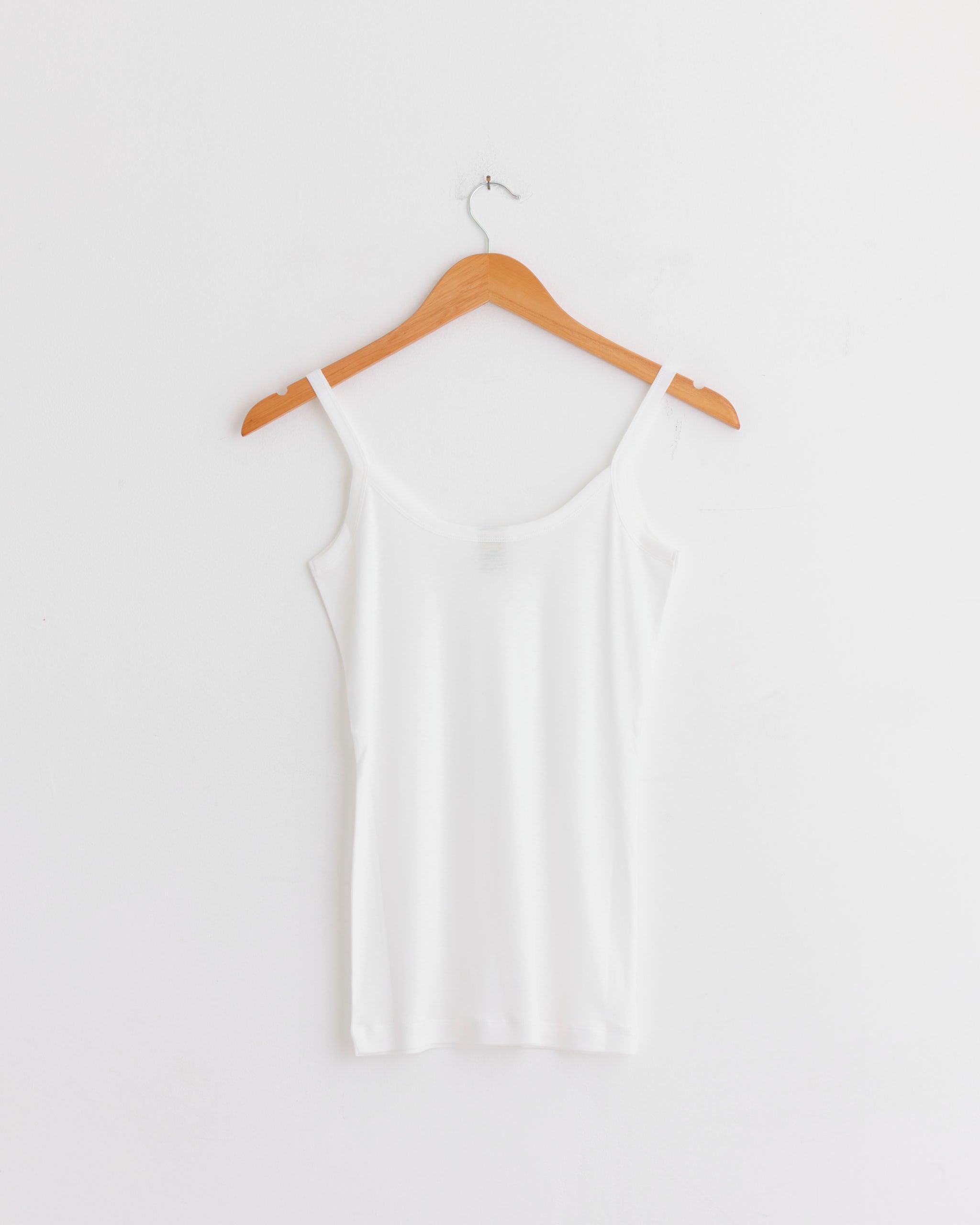 The FLORE FLORE Isla Cami in White hangs on a wooden hanger against a white wall.