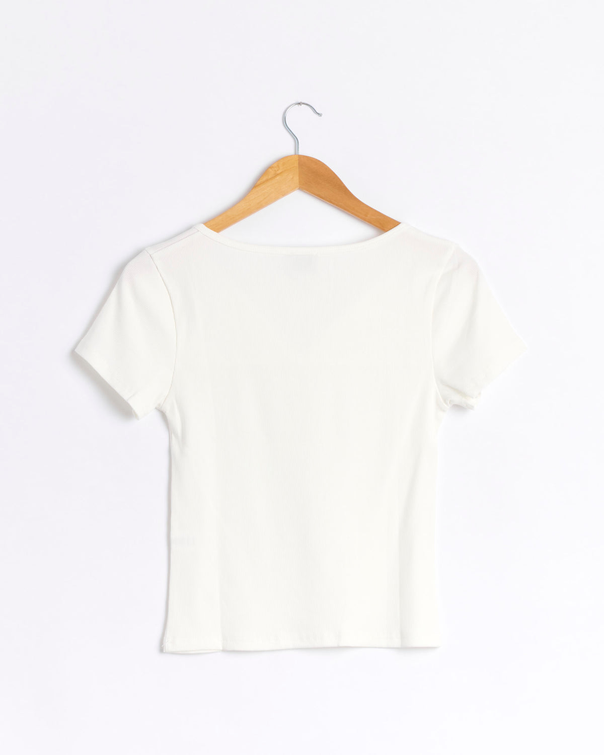 A short-sleeved, white ribbed jersey Tie Back Tee by Deiji Studios is displayed from the back, hanging on a wooden hanger against a plain white background. Drawing inspiration from Deiji Studios’ minimal aesthetic, this elevated basic features subtle texture and timeless simplicity.