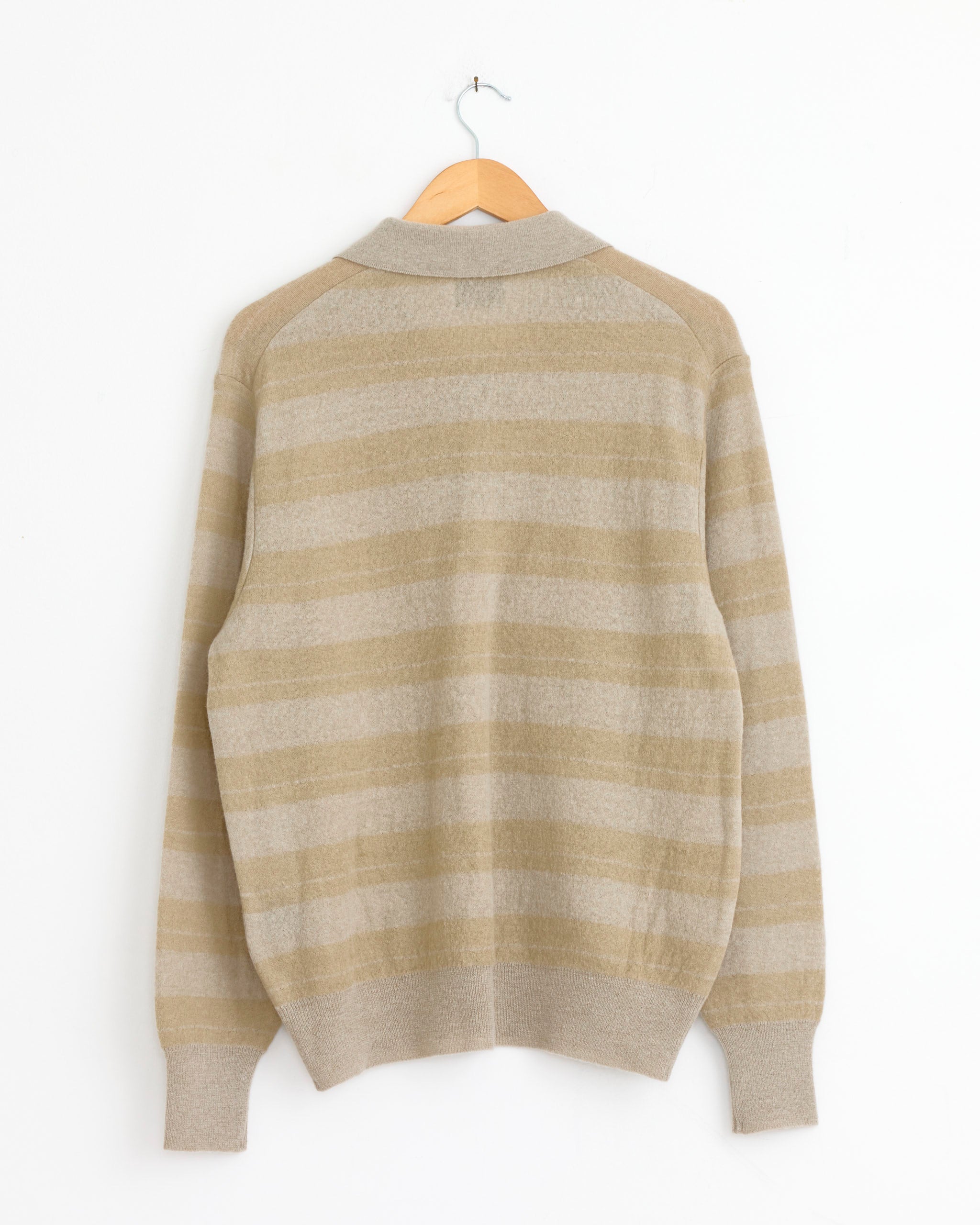 A ssstein Striped 1483 Sweater in Beige Grey Mix hangs on a wooden hanger against a white wall, displayed from the back. It features a ribbed collar, cuffs, and waistband.