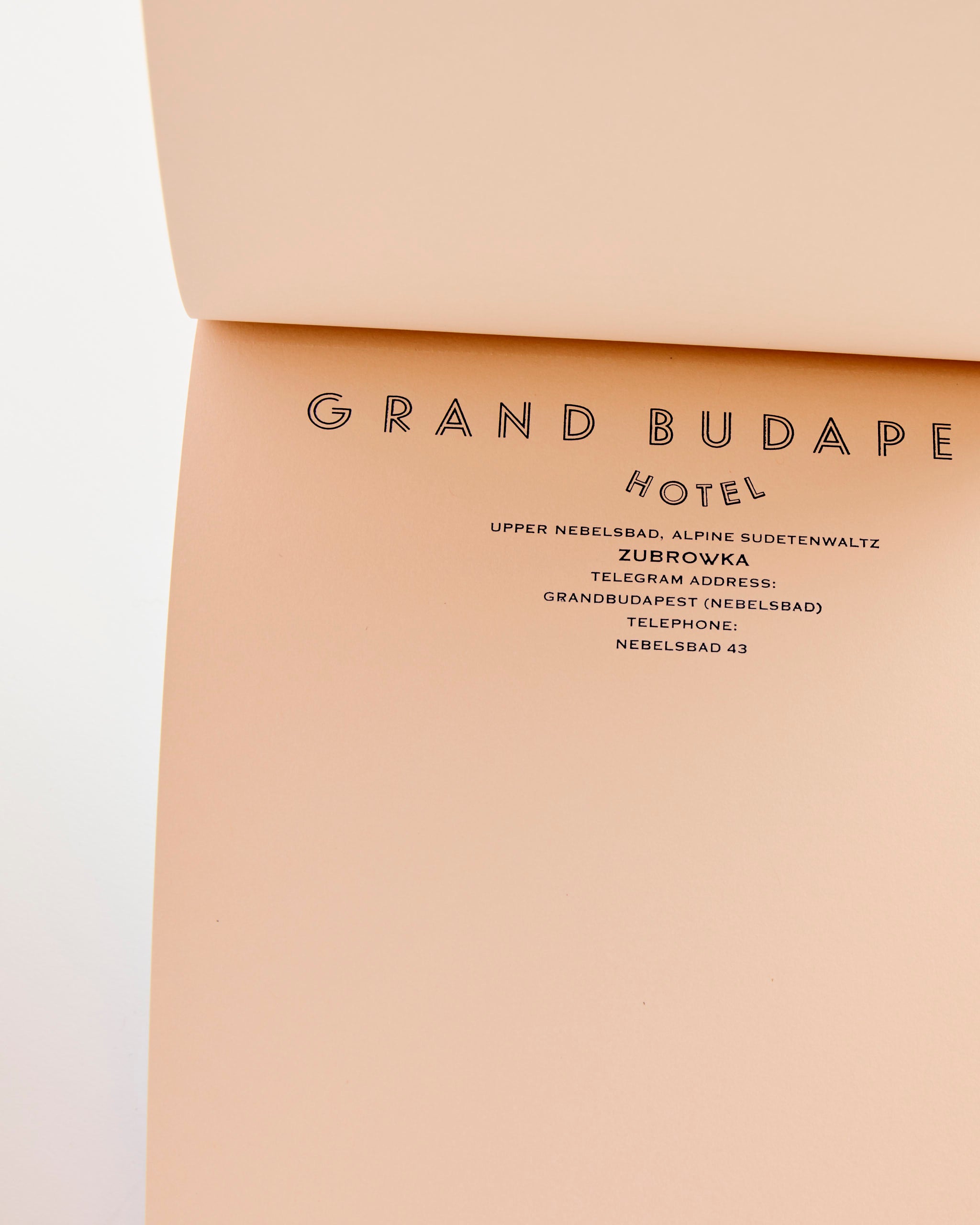 The Wes Anderson Letter Paper Notepad by Astier de Villatte is a peach-hued, art deco-inspired pad styled after GRAND BUDAPEST HOTEL stationery, complete with fictional address and contacts—a charming choice for creative correspondence.