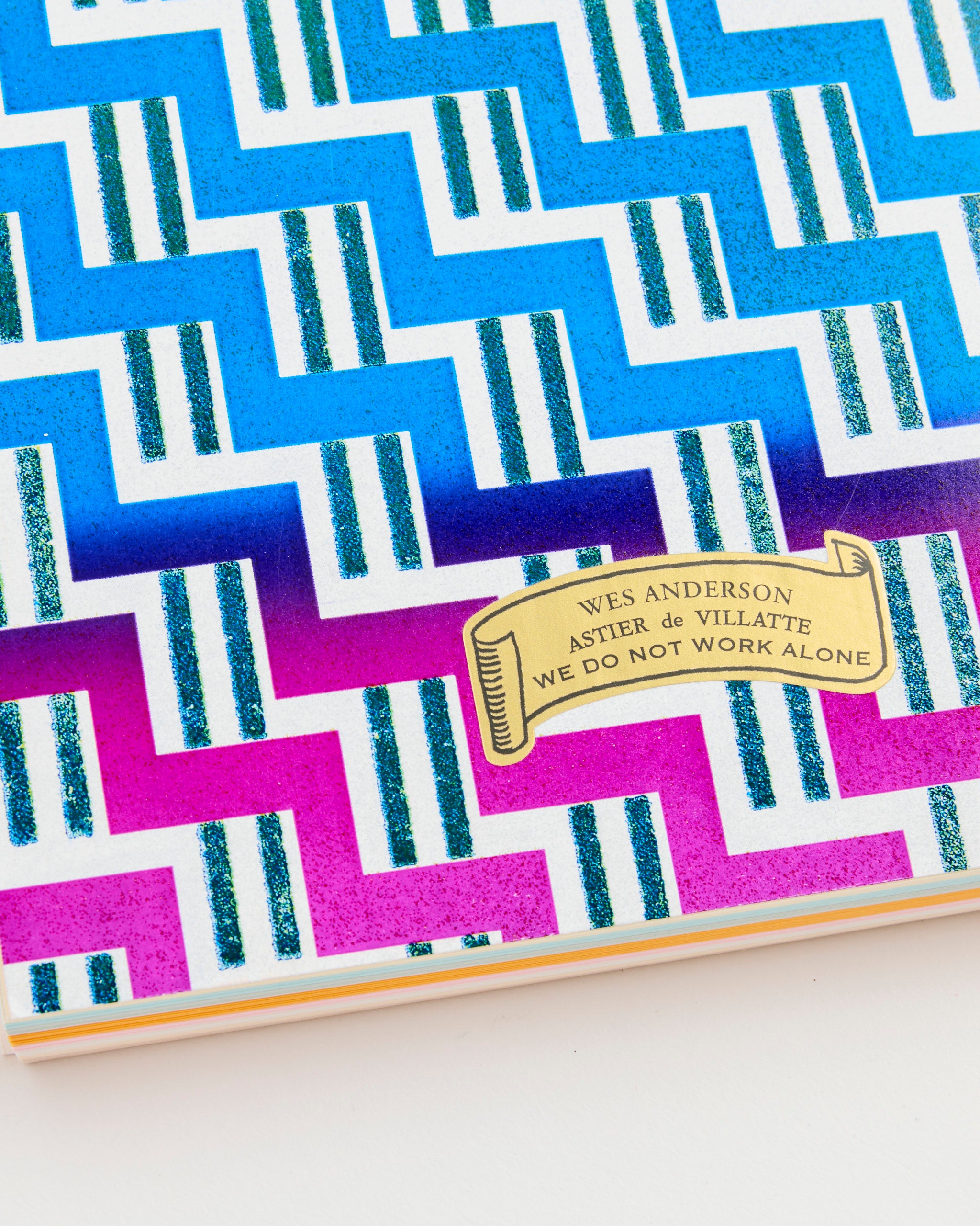 The Wes Anderson Letter Paper Notepad by Astier de Villatte features a bold blue and magenta zigzag design with glittery green lines and a yellow ribbon label reading: WES ANDERSON ASTIER DE VILLATTE WE DO NOT WORK ALONE.