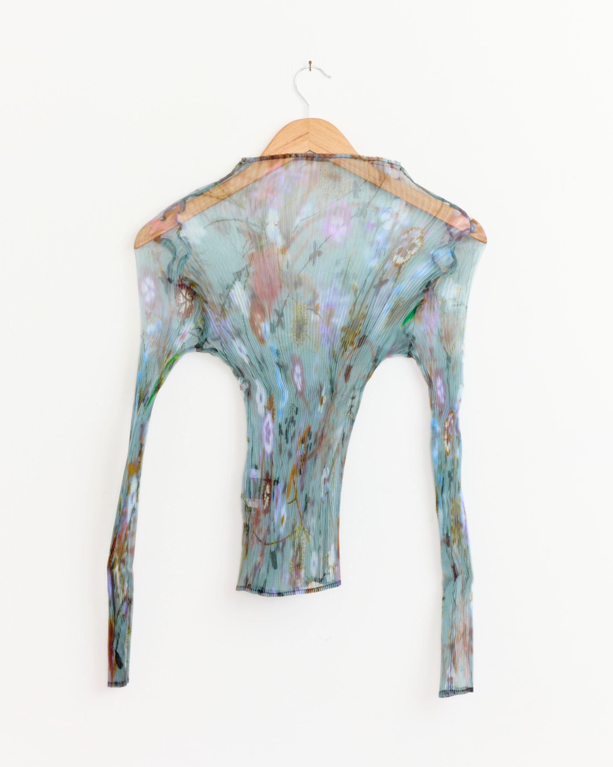 The Julia Heuer Lee Top in Frances, a semi-sheer long-sleeve blouse made from pleated crepe with a pastel floral print, hangs on a wooden hanger against a plain white background.