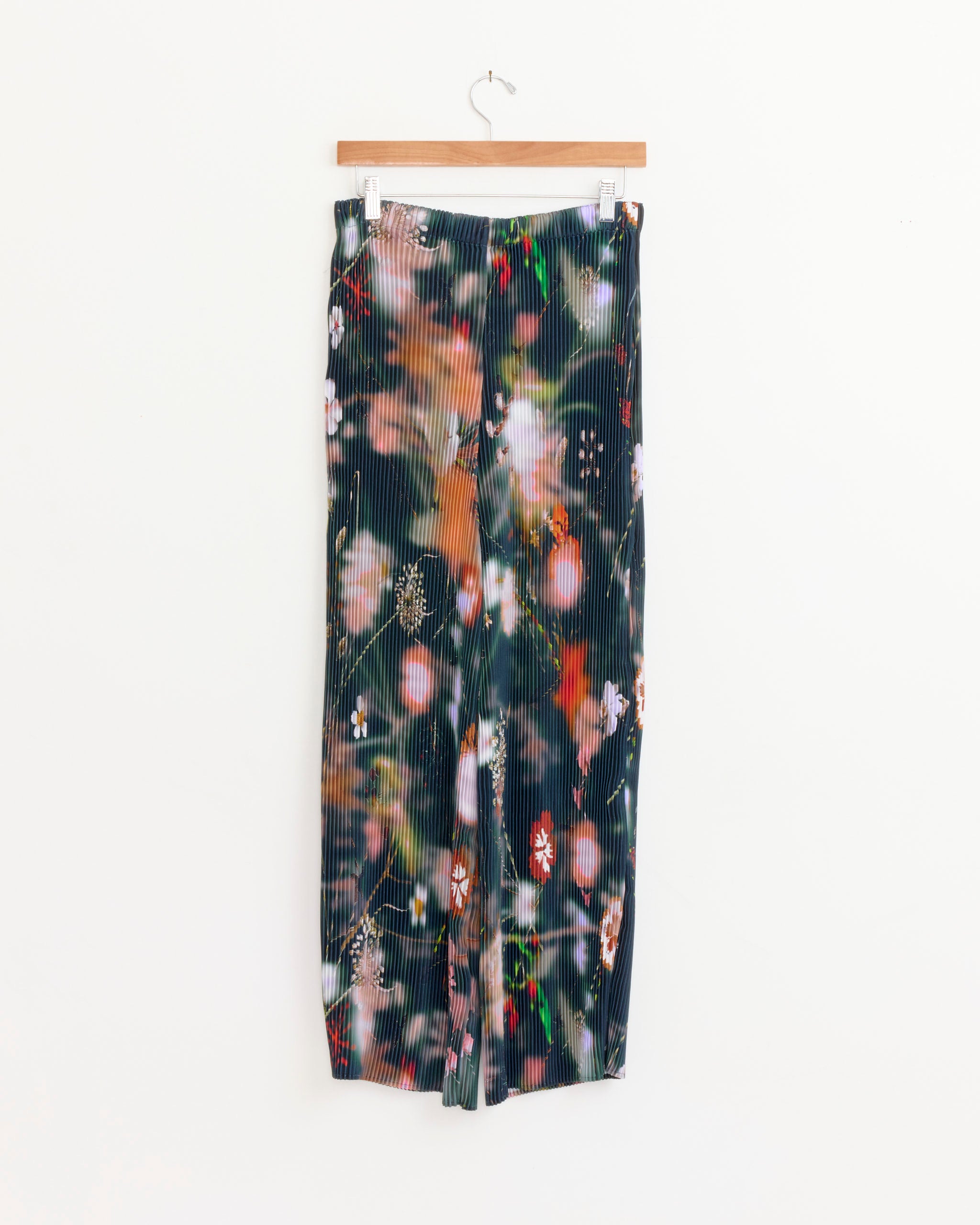 The Julia Heuer Jack Trouser in Frances features a hand-pleated, wide-leg silhouette and colorful abstract florals, displayed on a wooden hanger against a plain white background.