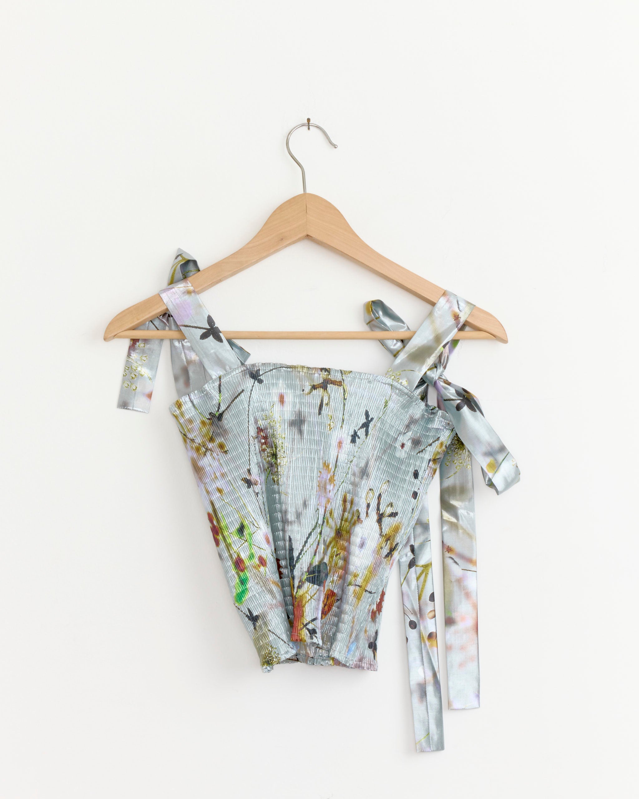 The June Metallic Top in Frances by Julia Heuer features pastel smock pleats, a nature-inspired print, and wide tie straps, shown on a wooden hanger against a plain white background.