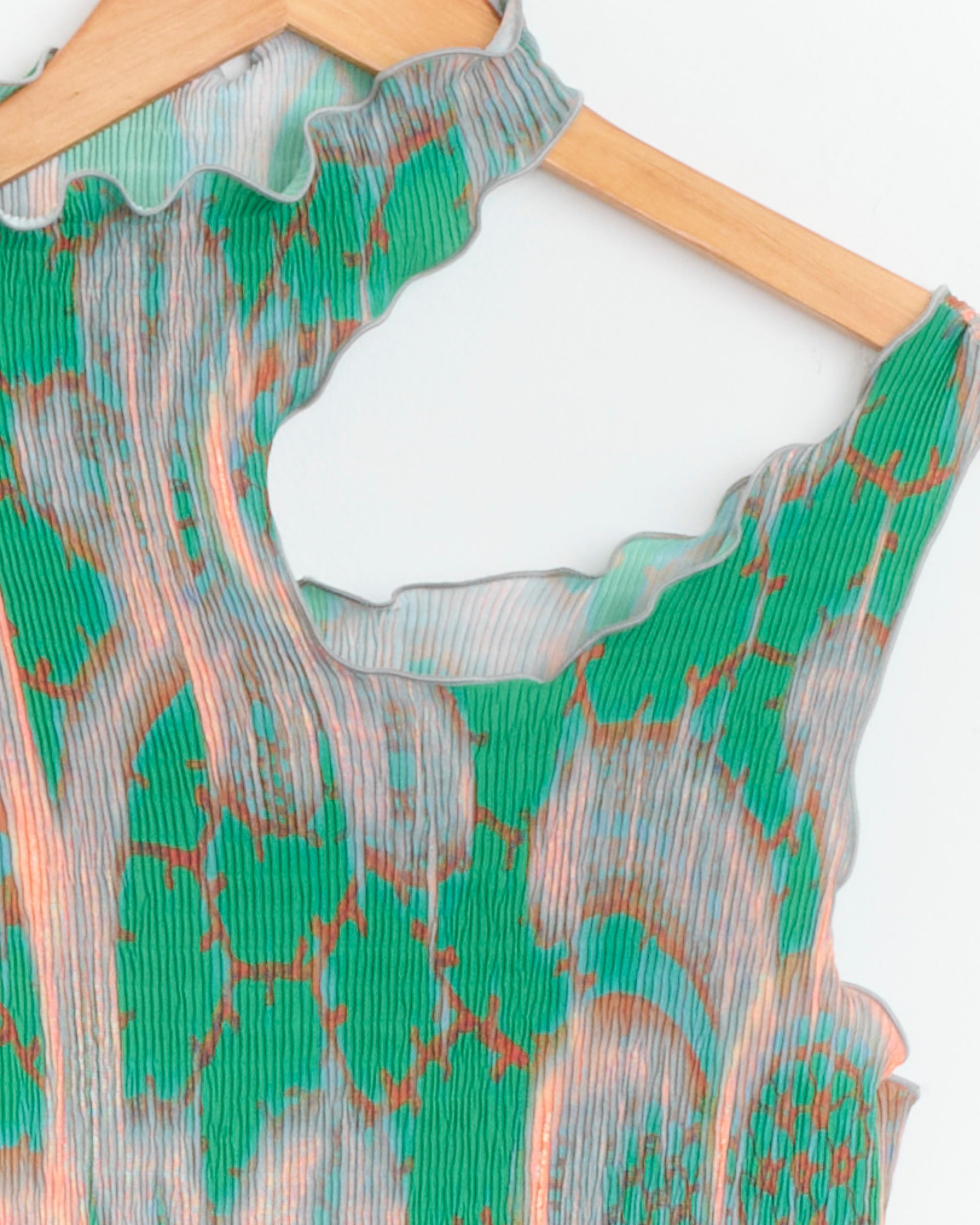 Close-up of the Tito Dress in Gallia by Julia Heuer, a sleeveless, garment-pleated polyester piece with sheer green and orange abstract stripes, wavy ruffled neckline and armholes, shown on a wooden hanger.