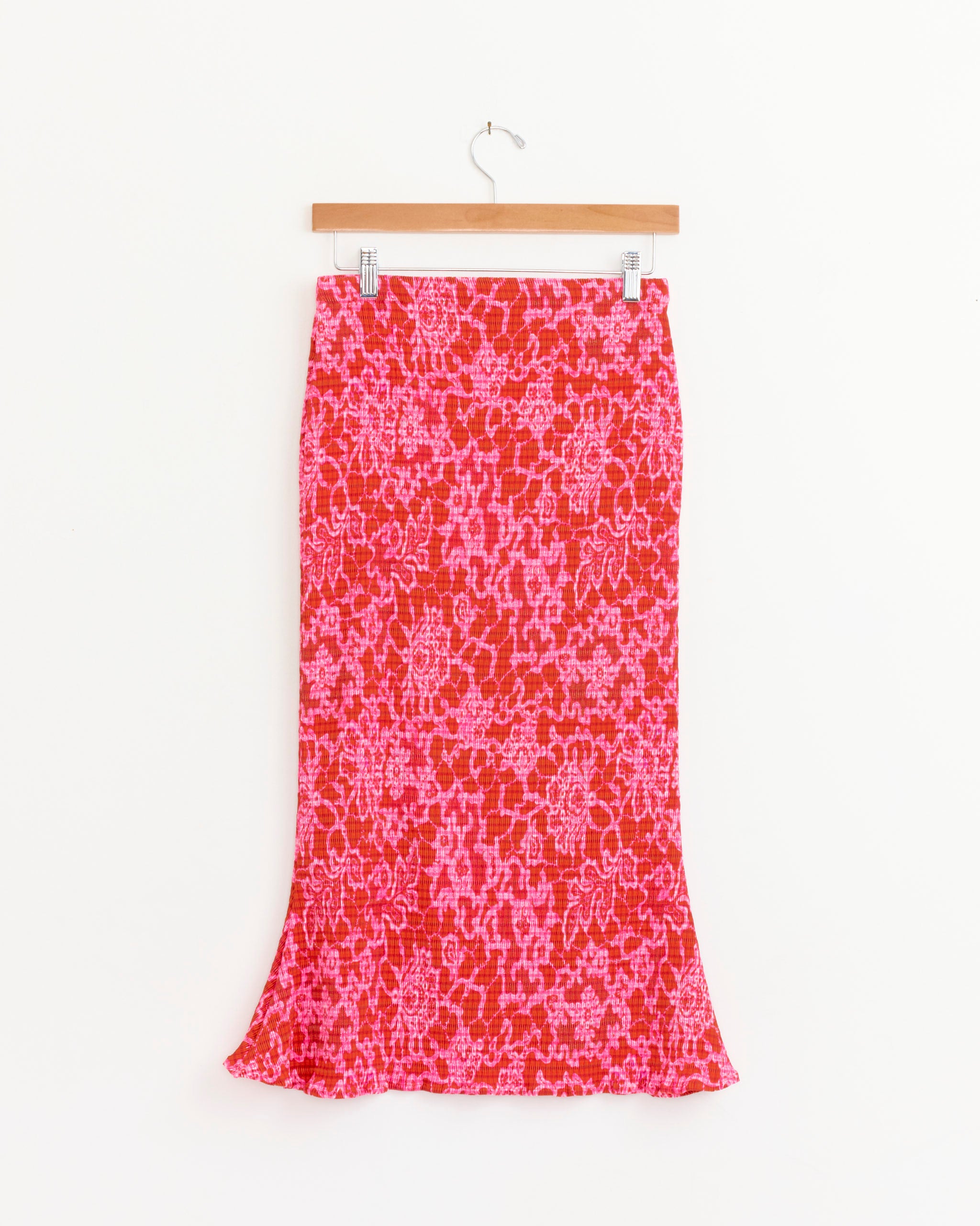 The Finn Skirt in Sansa by Julia Heuer, featuring a pink and red floral pattern, is displayed on a wooden hanger against a plain white background.