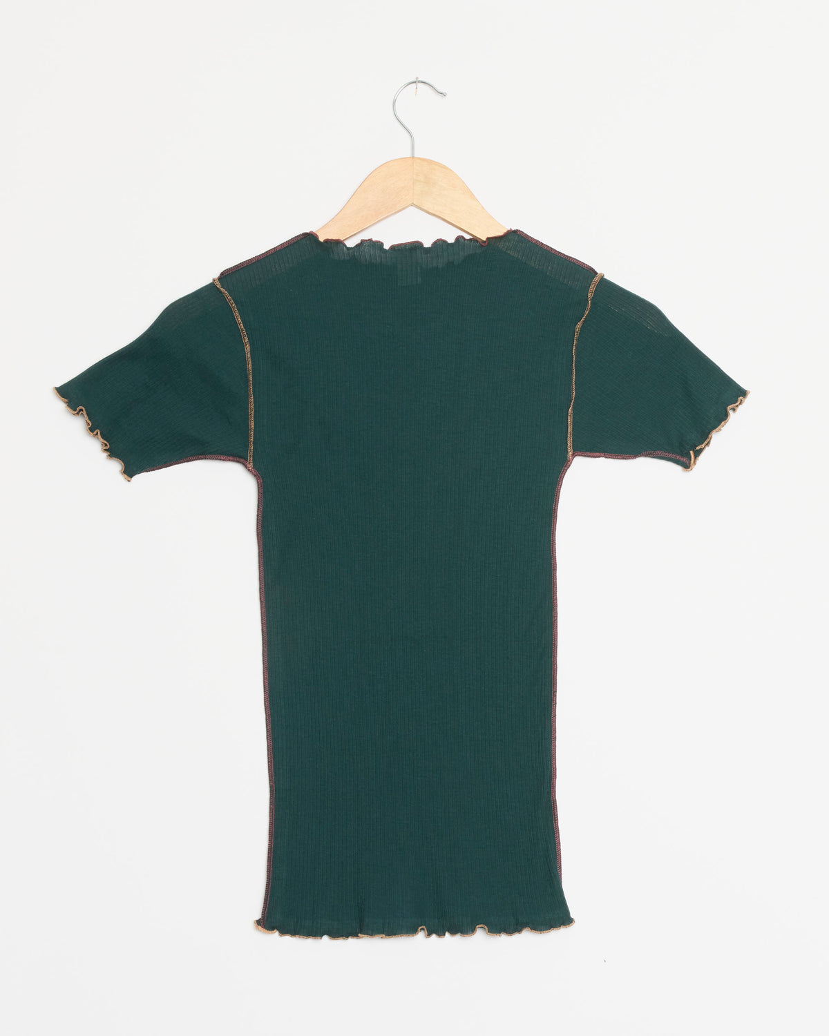 The Baserange Vein Tee Shirt in Hirsu Green, a dark green short-sleeve ribbed organic cotton dress featuring contrasting stitching and lettuce hem edges characteristic of Baserange’s signature style, is displayed on a wooden hanger against a white background.