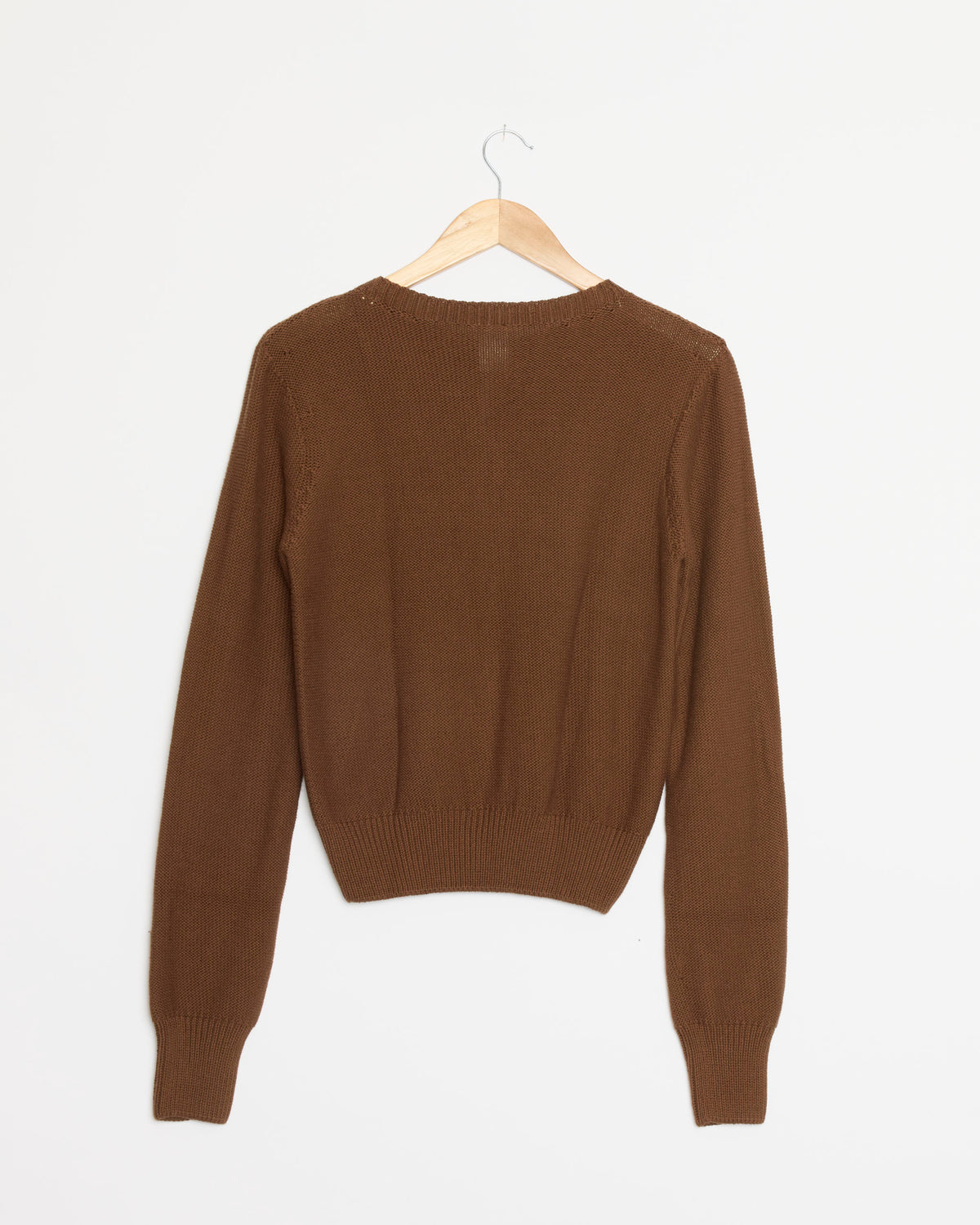 The Baserange Tier Cardigan in Nocciola Brown, crafted from organic cotton, is elegantly displayed from the back with its long sleeves draped over a wooden hanger against a plain white background.