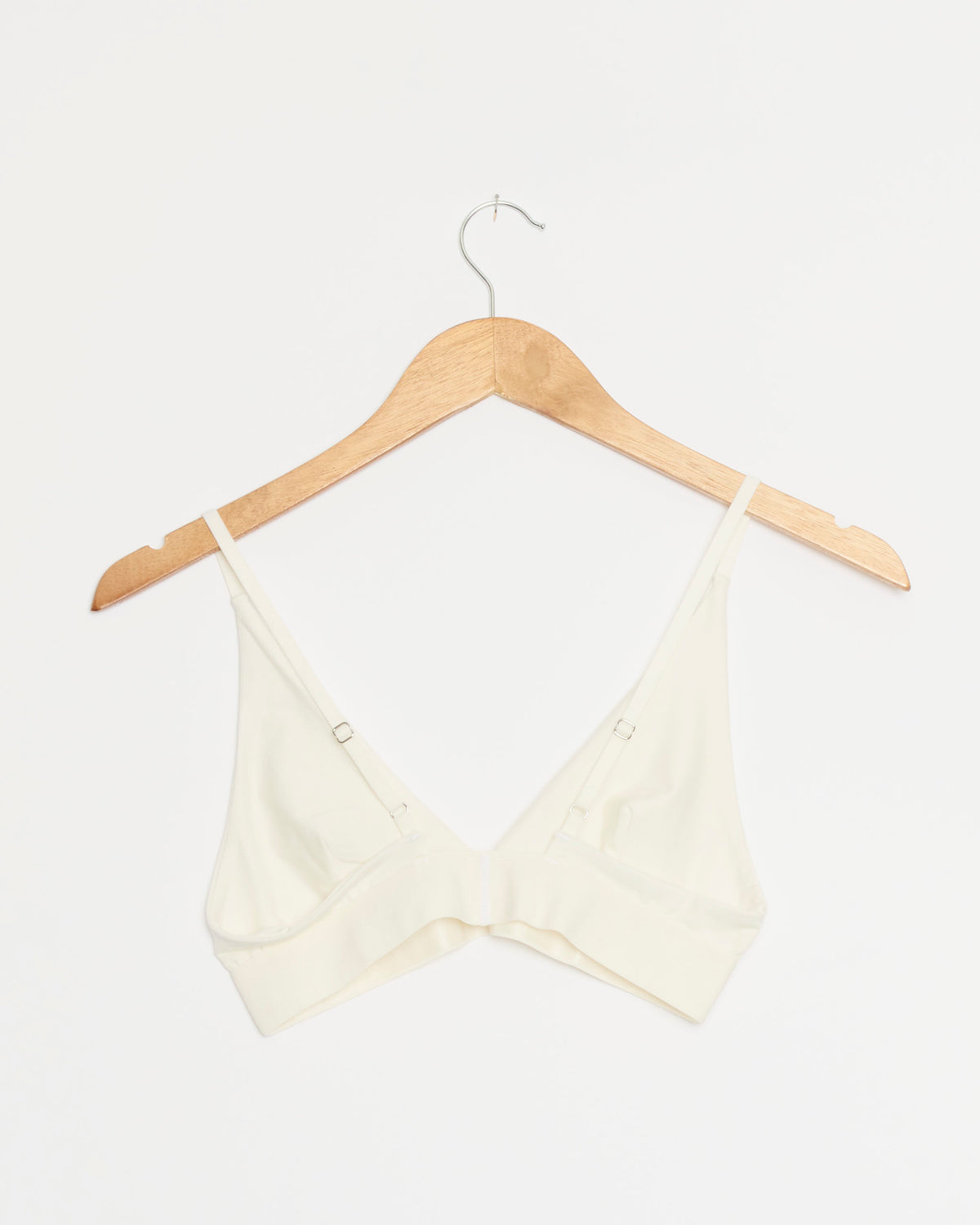 The Baserange Triangle Bra in Undyed, featuring thin adjustable straps, hangs on a wooden hanger against a plain white background.