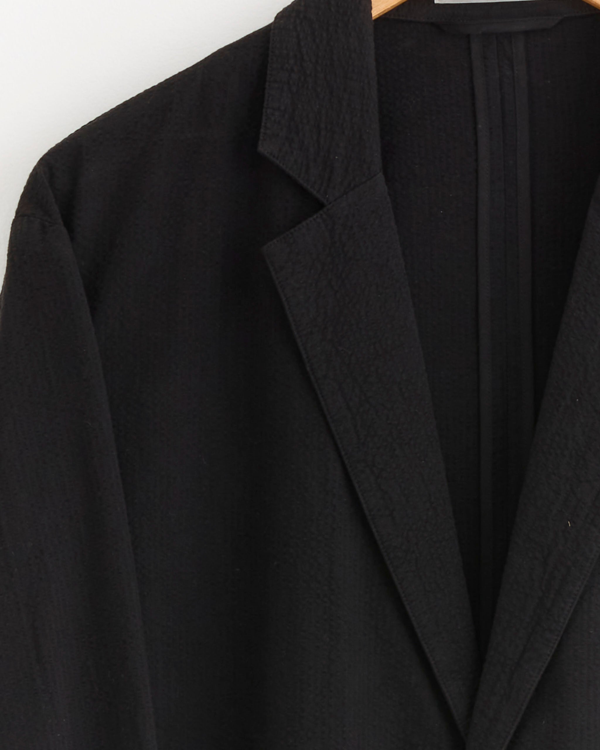 Close-up of the SMOCK Blazer in Japanese Seersucker Black, shown on a wooden hanger against a white background. Only the collar and lapel of this lightweight blazer are visible.