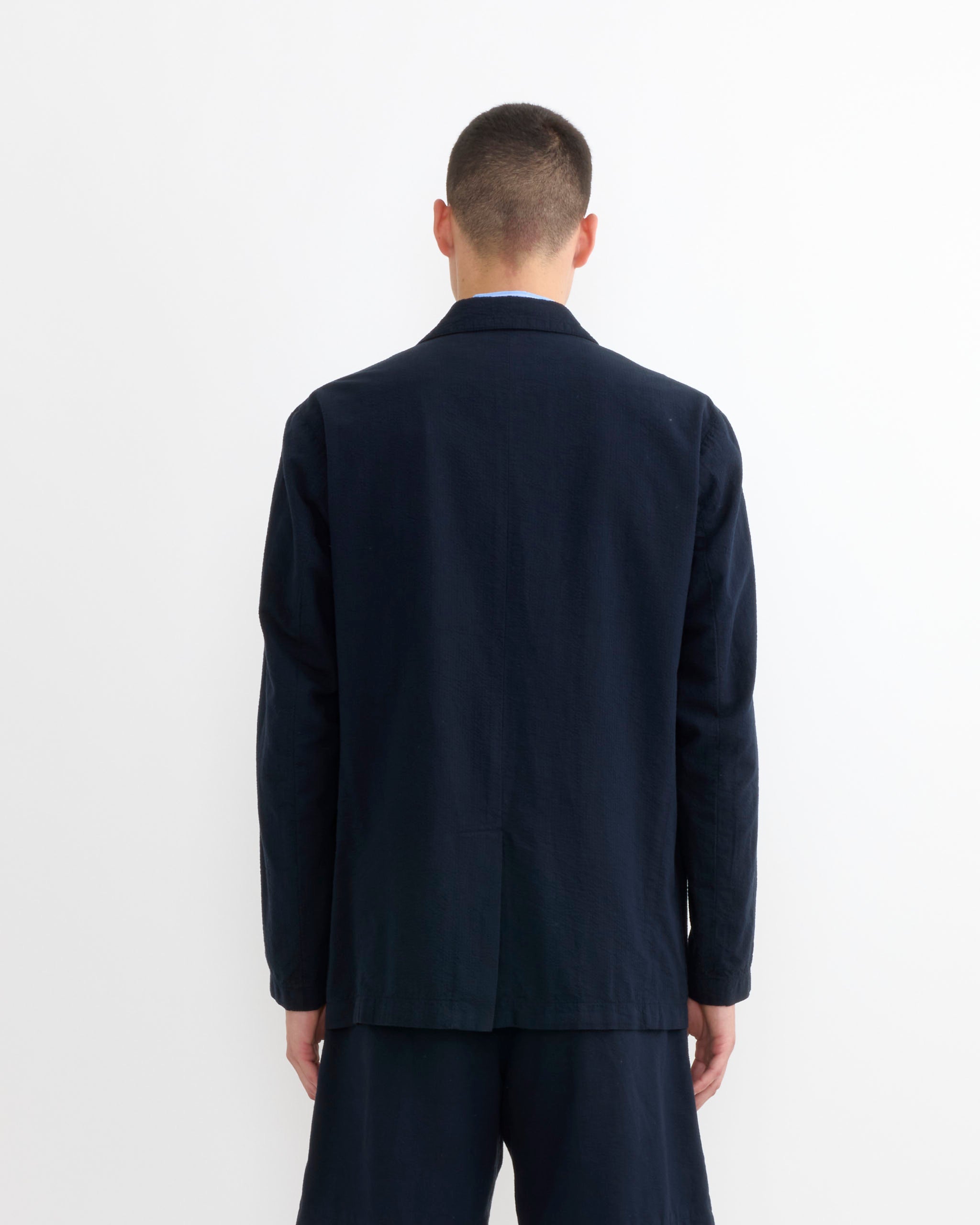 A person with short hair, seen from behind, wears the SMOCK Blazer in Japanese Seersucker Navy and matching shorts against a plain white background.