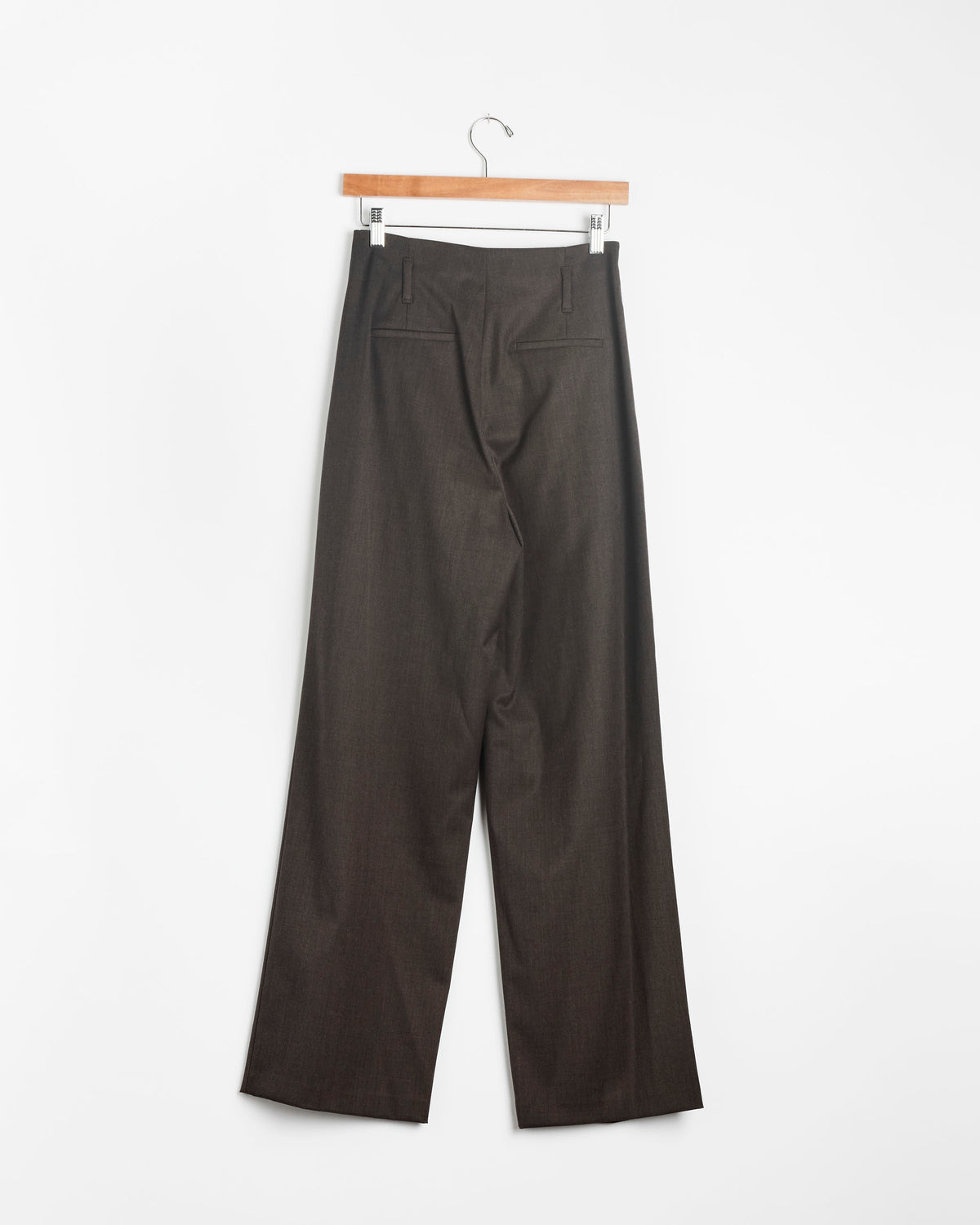 The Amomento Straight Tuck Pant in Brown, displayed from the back on a wooden hanger against a plain white background, features belt loops, two back pockets, and a relaxed wide-leg silhouette.