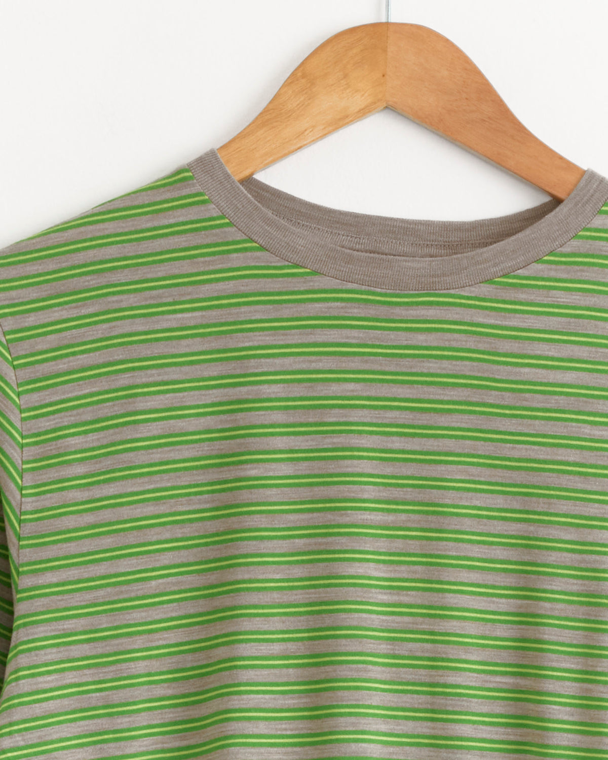 Soft Wool Jersey Long Sleeve Tee in Green Stripe by Auralee hanging on a wooden hanger.