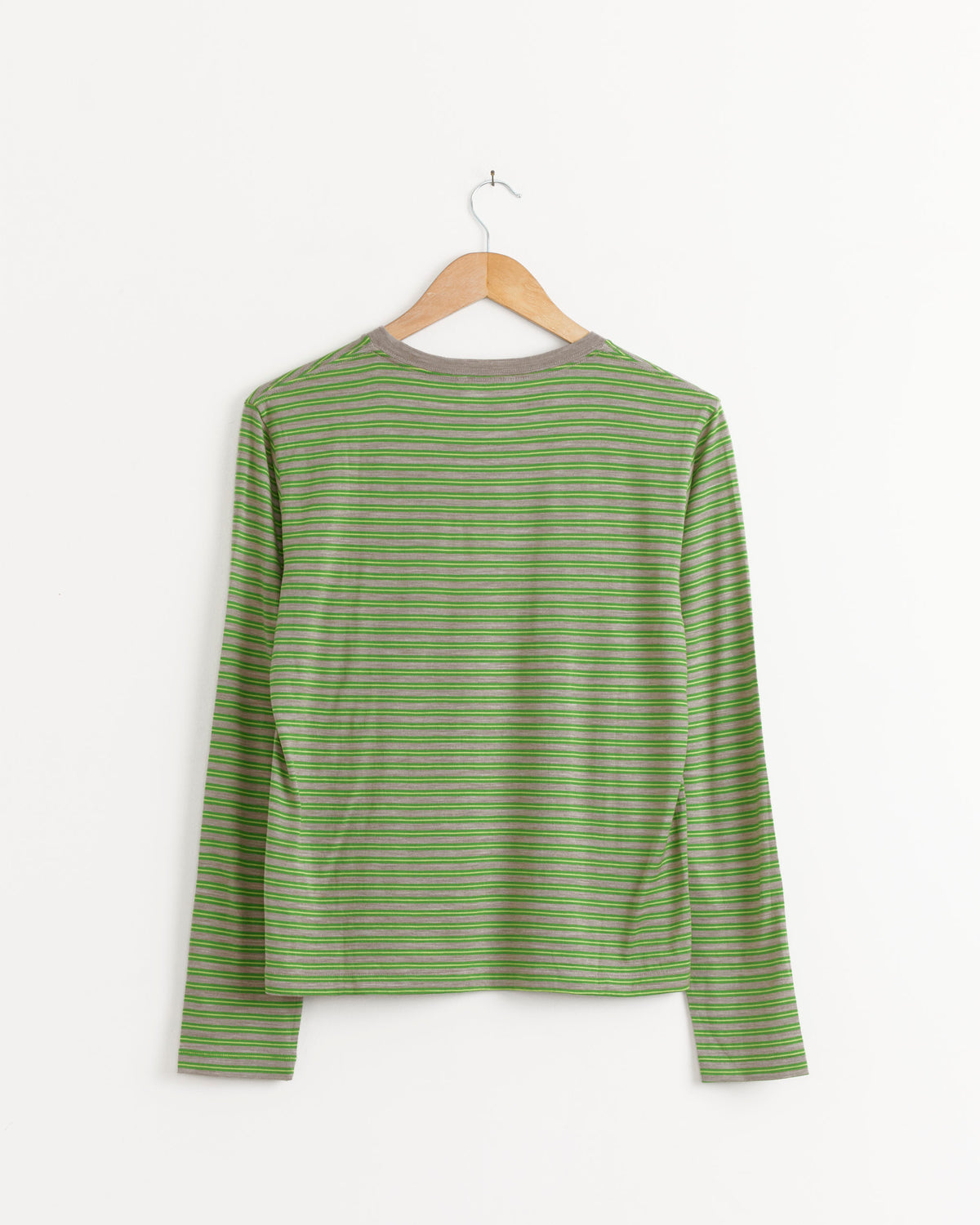 Auralee Soft Wool Jersey Long Sleeve Tee in Green Stripe with green and grey horizontal stripes, hanging on a wooden hanger against a white wall.