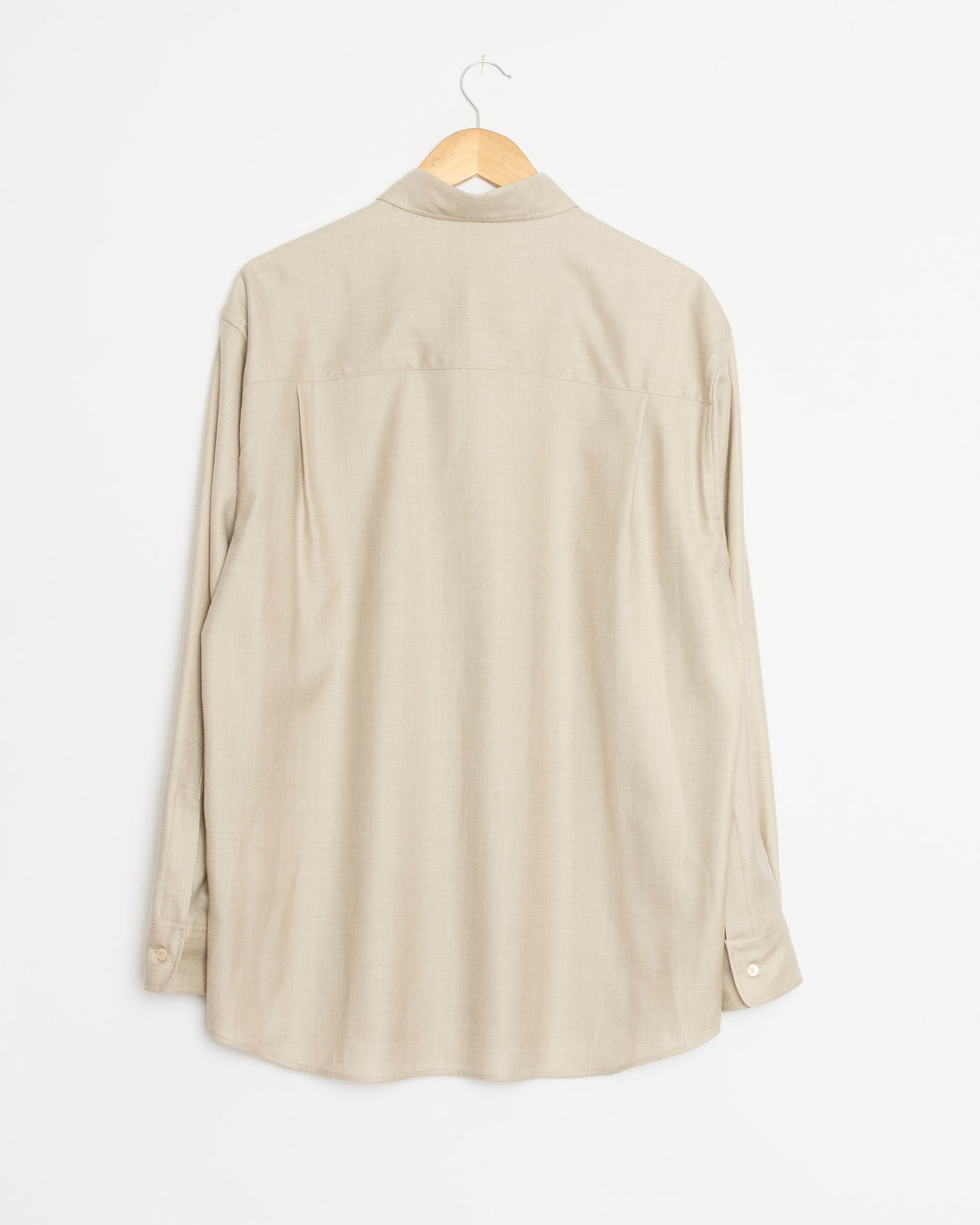 An Auralee Super Light Wool Shirt in Top Beige is displayed from the back, hanging on a wooden hanger against a plain white background. Crafted in Japan from premium wool, this long-sleeve button-up showcases refined simplicity and outstanding craftsmanship.