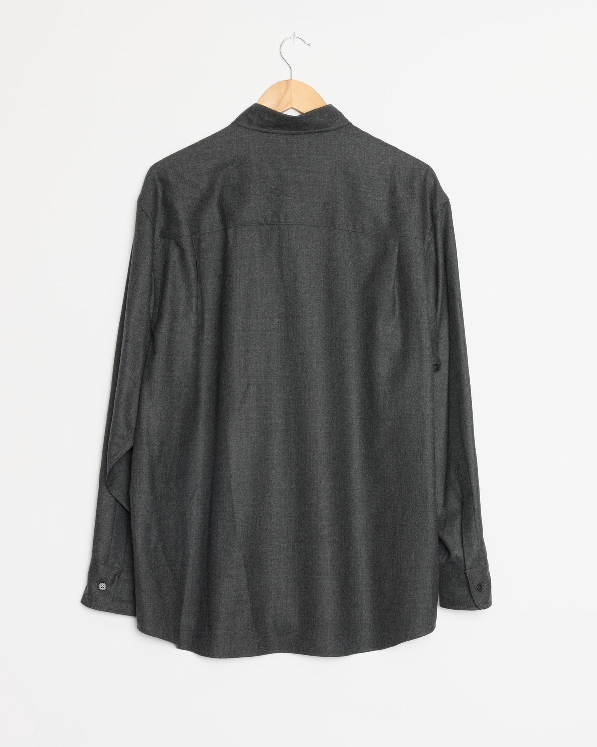 An Auralee Super Light Wool Shirt in Top Charcoal hangs on a wooden hanger against a plain white background. Made in Japan from premium wool, this long-sleeve button-up shirt combines timeless style with exceptional craftsmanship.