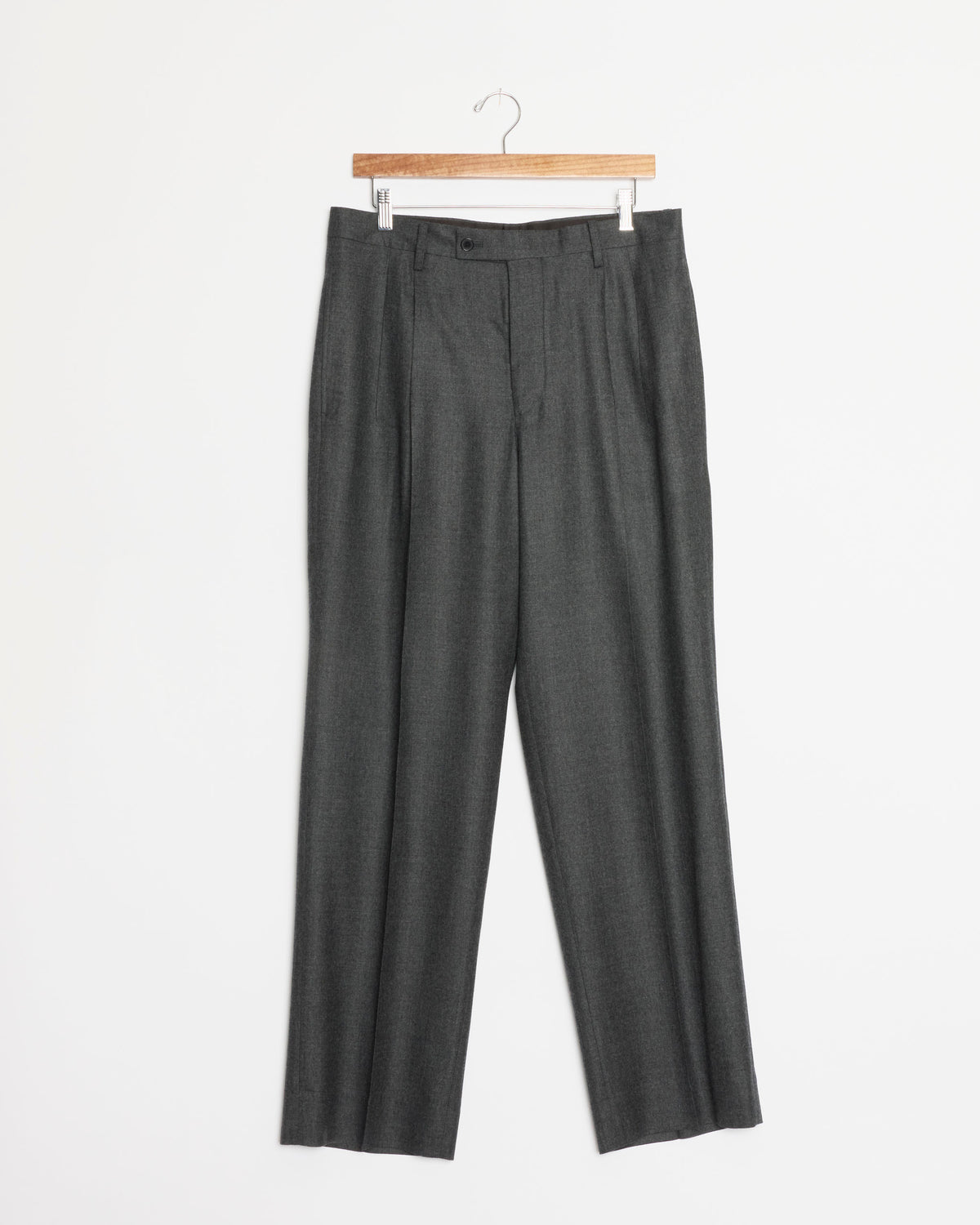 The Super Light Wool Two Tuck Slack in Top Charcoal by Auralee hangs on a wooden hanger against a plain white background; these expertly crafted wide-leg trousers are made in Japan.