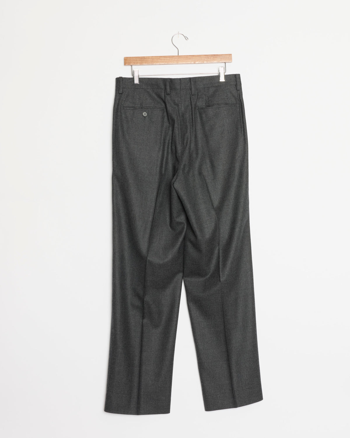 A pair of Auralee Super Light Wool Two Tuck Slack wide leg trousers in Top Charcoal, hanging on a wooden hanger against a plain white background, shown from the back.
