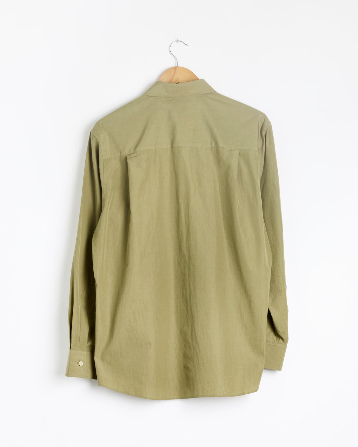 An Auralee Finx Light Weather Chambray Shirt in Olive Brown hangs on a wooden hanger, displayed with the back facing forward against a plain white background.