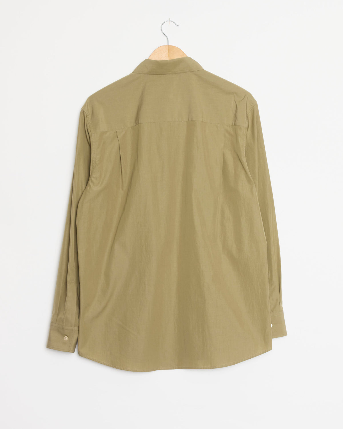 An Auralee Finx Light Weather Chambray Shirt in Olive Brown, featuring long sleeves, hangs on a wooden hanger against a white background, displayed from the back. Expertly crafted in Japan, it highlights refined craftsmanship and effortless style.