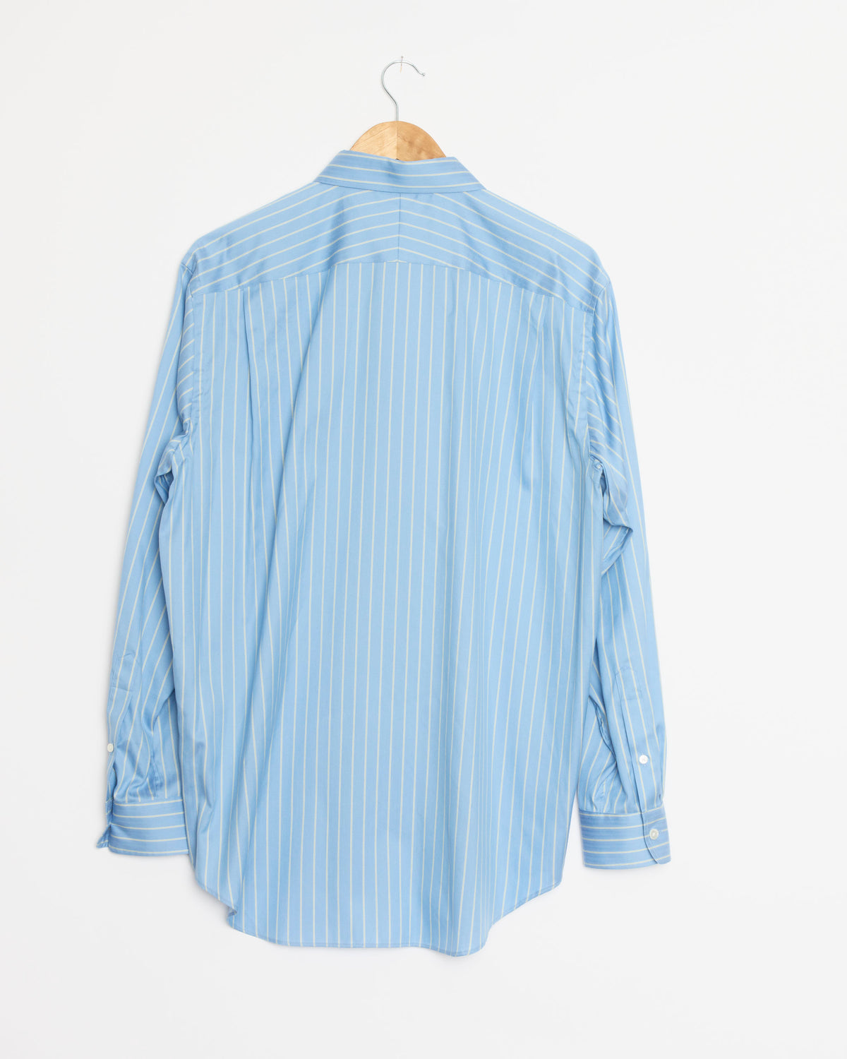 AURALEE’s Cotton Silk Stripe Shirt in Sax Blue, expertly crafted from premium Egyptian Giza cotton and adorned with white vertical stripes, is displayed from the back on a wooden hanger against a plain white background.