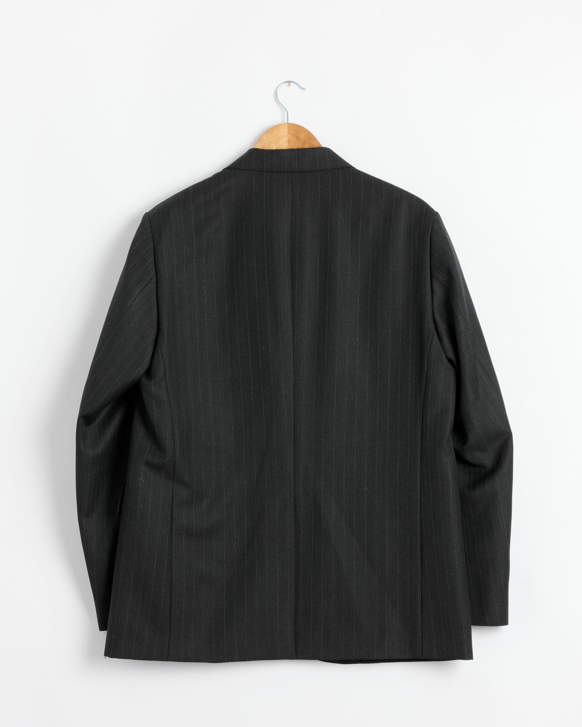 Back view of the Auralee Bluefaced Wool Jacket in Charcoal Navy Stripe, crafted from Super 130’s Merino wool and made in Japan, hanging on a wooden hanger against a plain white wall.