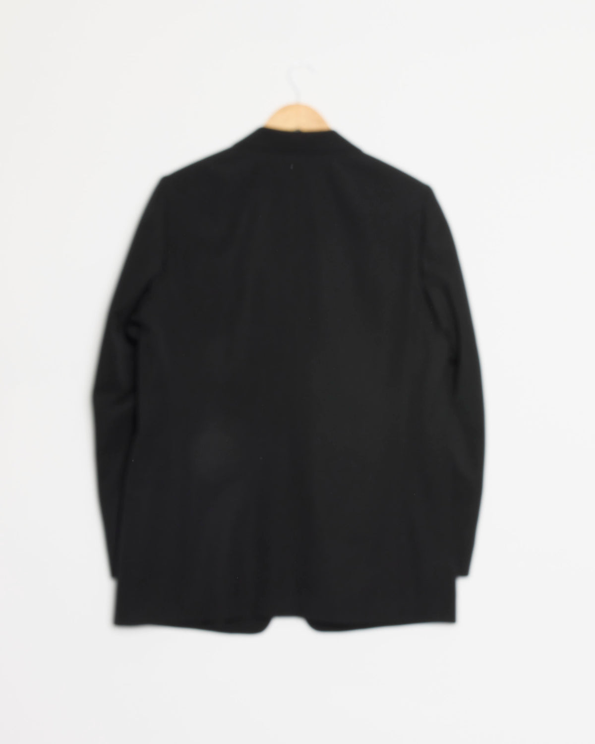 The Light Wool Max Gabardine Jacket in Top Black by Auralee hangs on a wooden hanger against a plain white background, displayed from the back. Expertly crafted in Japan, this piece showcases timeless style and exceptional craftsmanship.