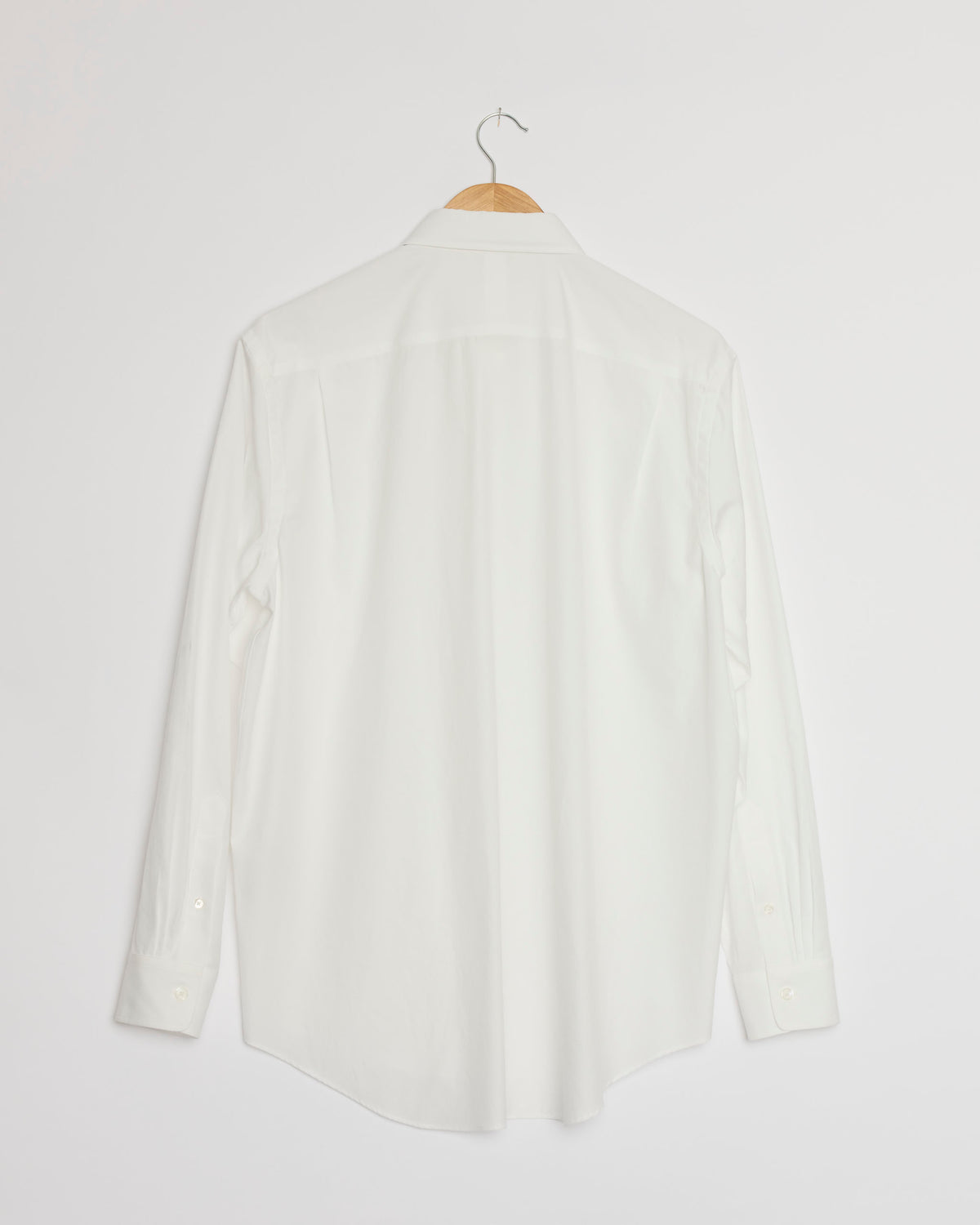 The Washed Finx Twill Shirt in White by Auralee, crafted from premium Egyptian cotton, is displayed from the back on a wooden hanger against a white background.