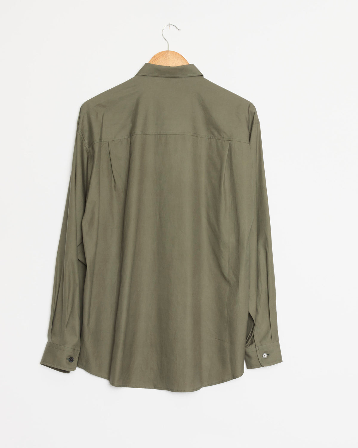 A Dark Olive Washed Finx Twill Big Shirt by Auralee, made from premium Egyptian cotton with a distinctive washed twill texture, hangs long-sleeved on a wooden hanger against a plain white wall, displayed from the back.