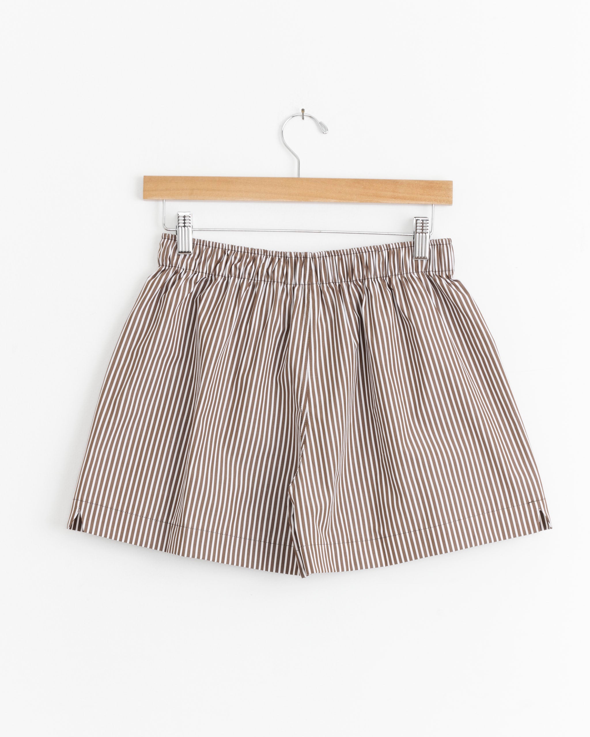 La Boxer Classica in Cortado Stripe by Comme Si: beige shorts with thin black stripes and an elastic waistband, shown on a wooden hanger against a white background—ideal for luxury loungewear or men’s sleepwear.