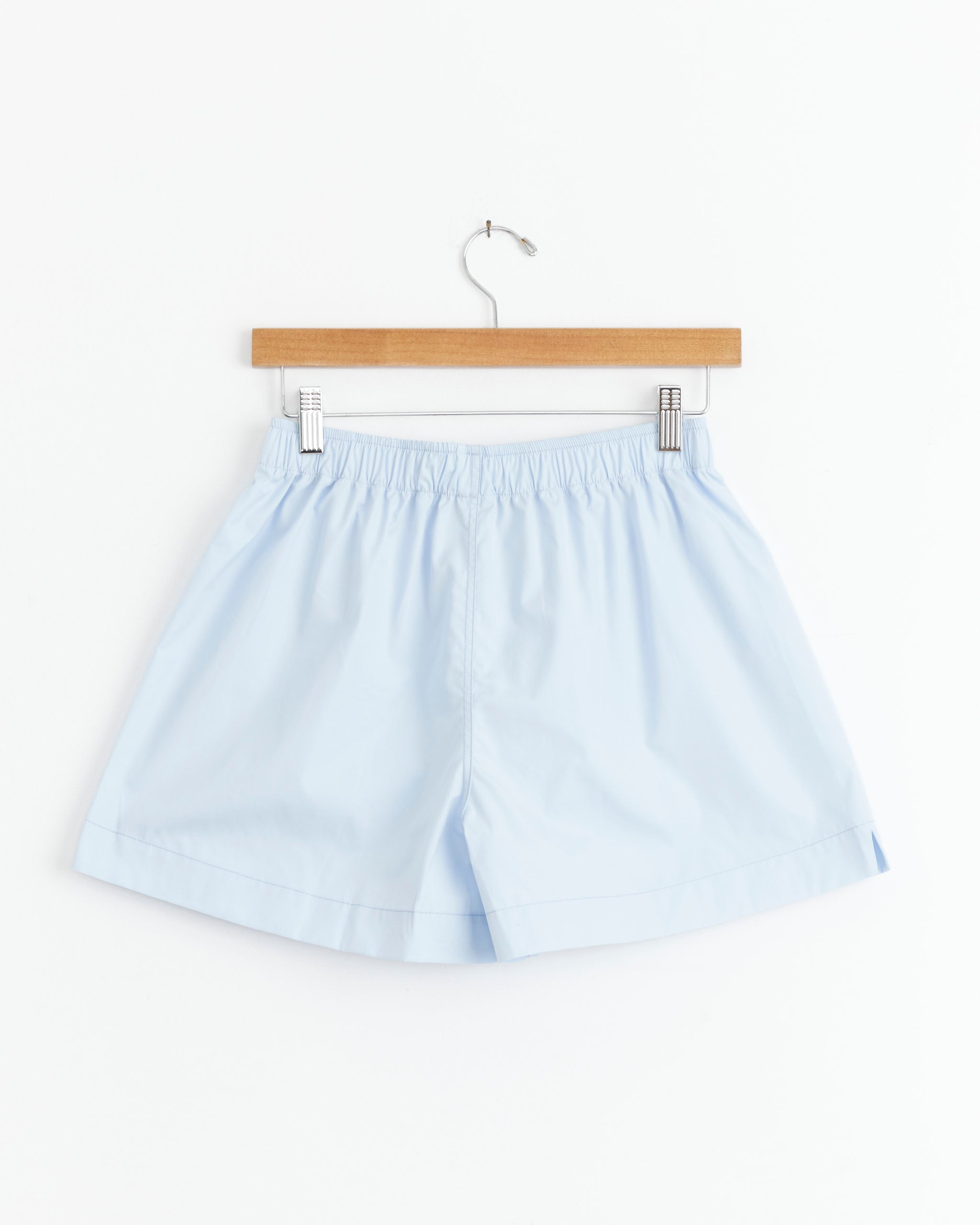 La Boxer Classica in Marina by Comme Si—light blue men's loungewear shorts with an elastic waistband, displayed on a wooden hanger against a plain white background.