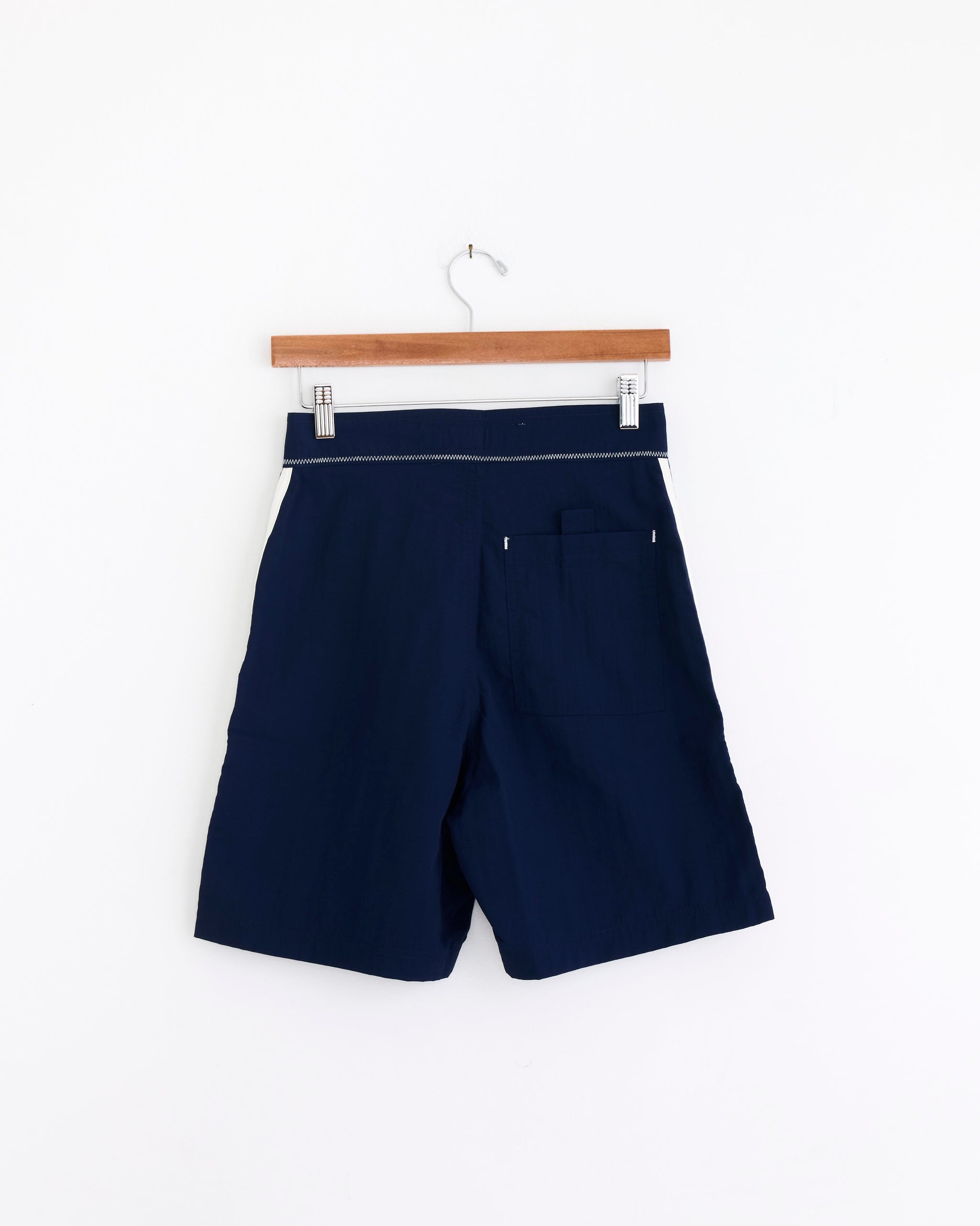 The Long Short in Navy/White by Made Some Sportswear features a vintage-inspired sporty look with an elastic waistband and a single back pocket, displayed on a wooden hanger against a plain white background.