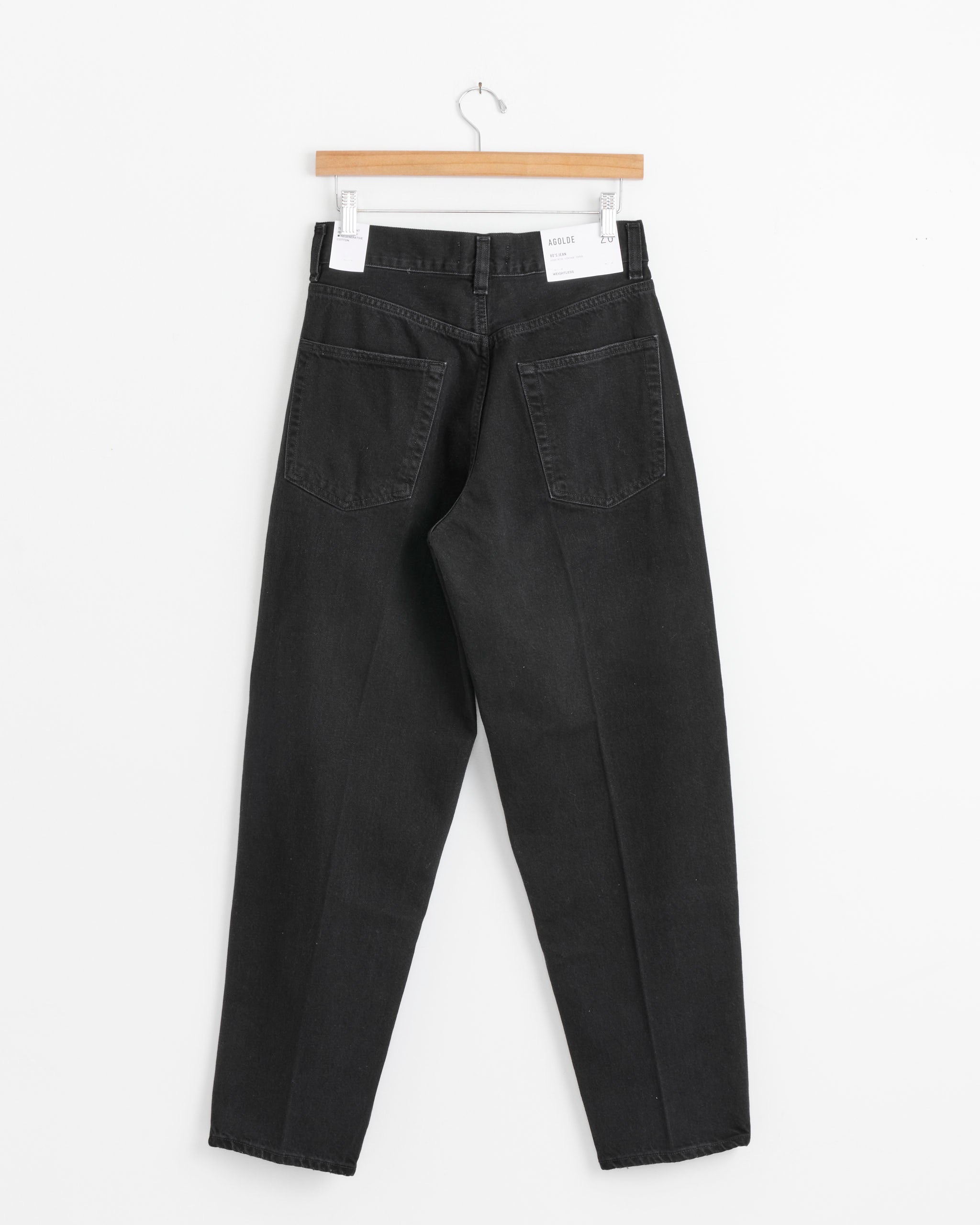 The AGOLDE 80s Jean in Phase is displayed hanging on a wooden hanger against a white background, shown from the back with two rear pockets visible.