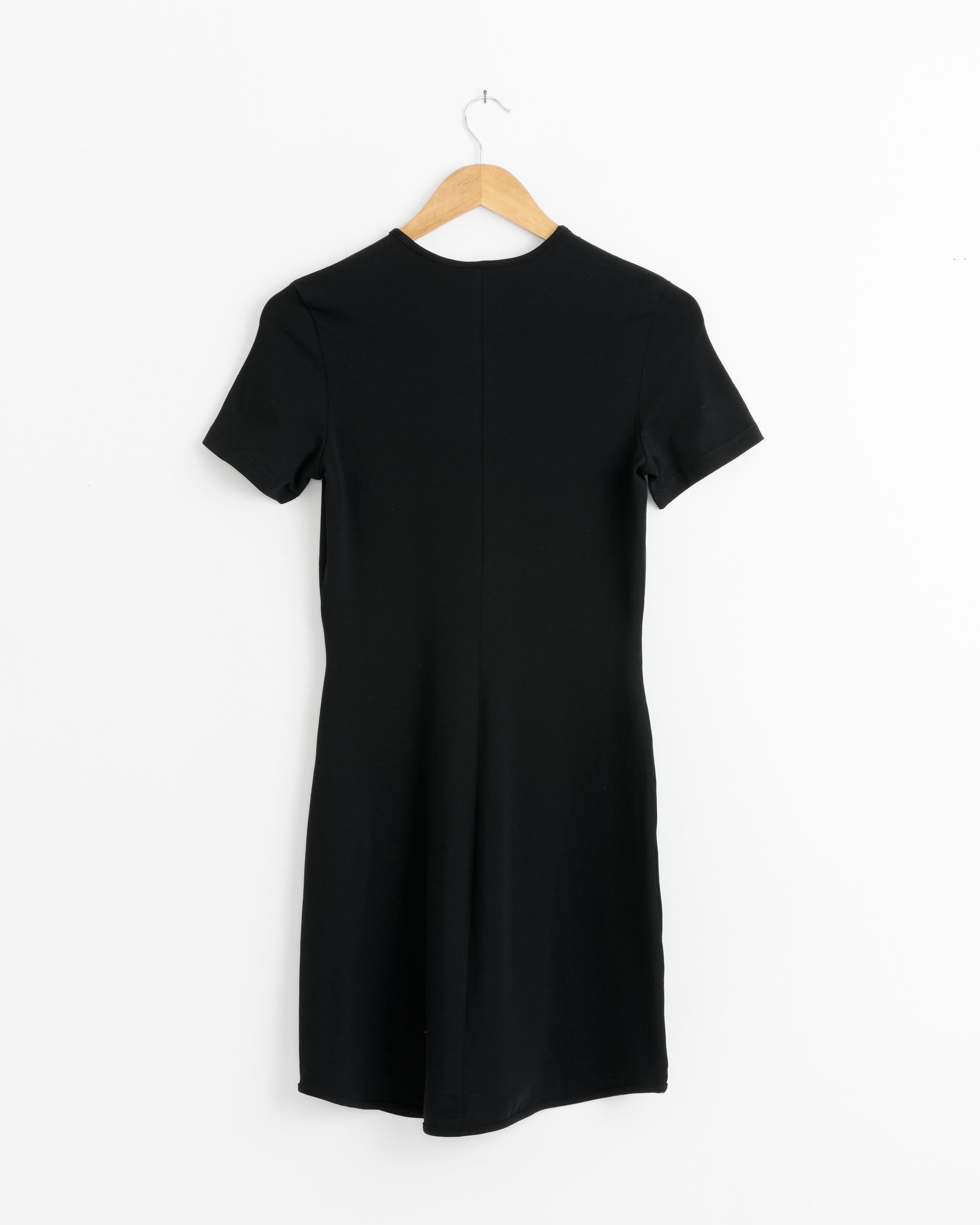 The Ying Yang Mini Dress in Black by J. Kim is a simple, fitted mini dress with T-shirt sleeves, shown on a wooden hanger against a white background. It features a clean design without patterns or embellishments.